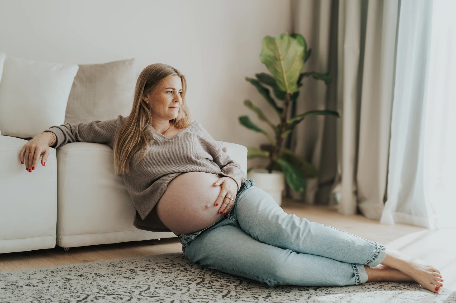 A mother-to-be relaxes indoors on the floor near a sofa in Dubai, showing a cozy lifestyle approach for indoor maternity photoshoots.