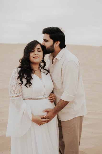 A close couple portrait shows an expecting mother and partner embracing on Dubai dunes during a maternity photoshoot at sunset.