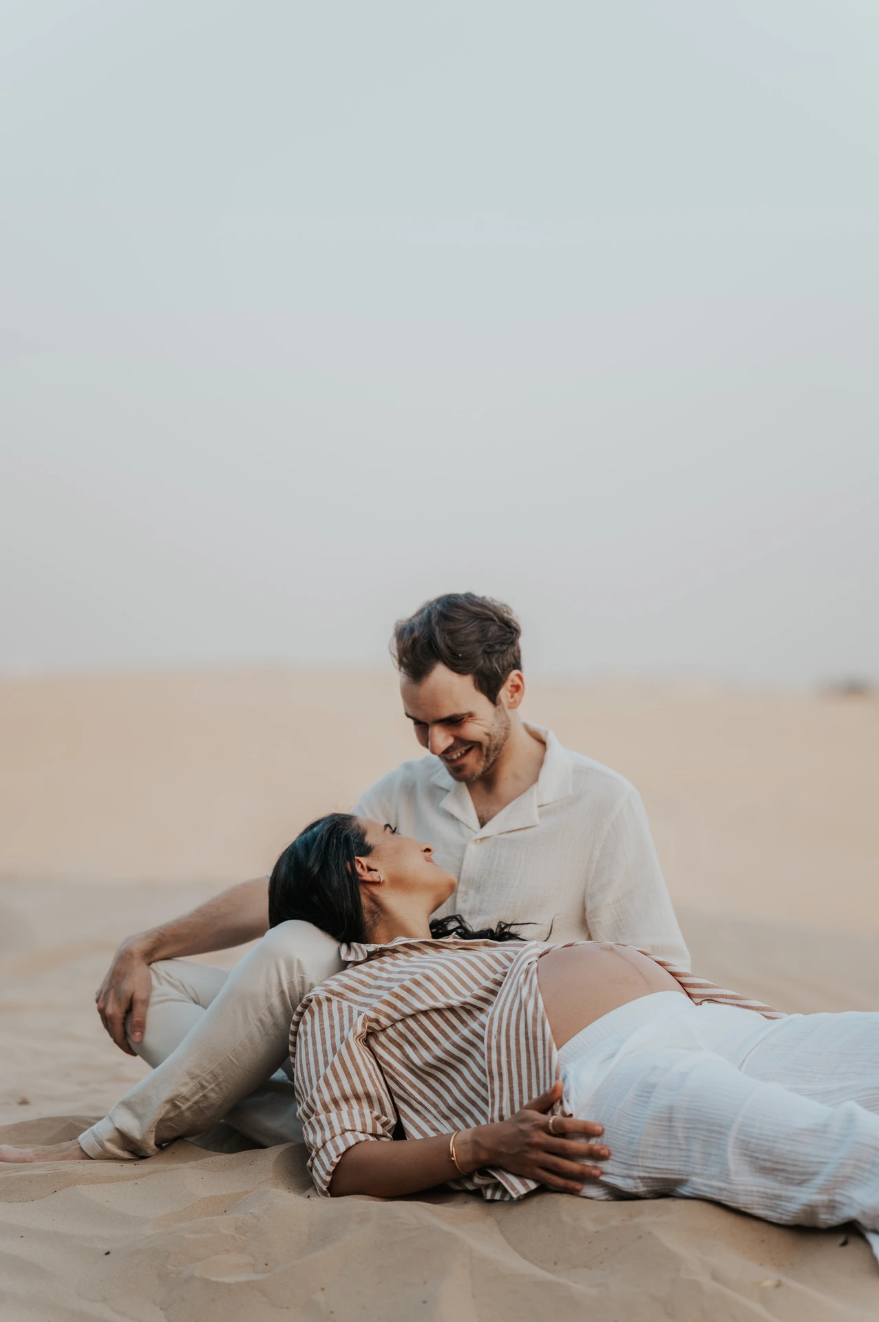 An expecting couple sits together on Dubai desert dunes during a maternity photoshoot, illustrating a warm and intimate desert session style.