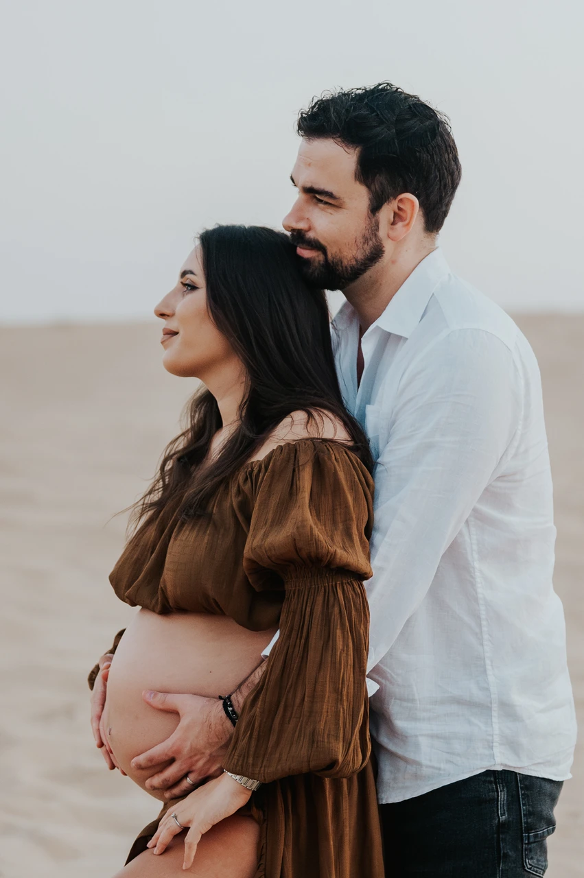 Planning desert maternity photoshoot Dubai - side embrace crop A side crop captures an expecting couple embracing on Dubai dunes during a maternity photoshoot, with focus on connection and body language.