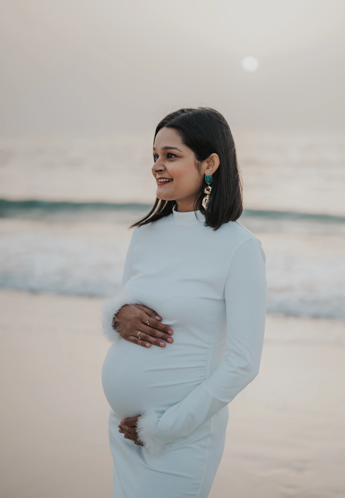 Close-up maternity portrait of an expecting mother in a white dress on Dubai beach, smiling softly during a calm seaside photoshoot.