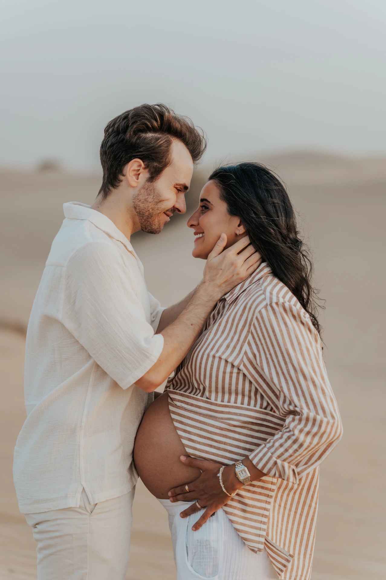 An expecting couple shares an intimate close-up on Dubai beach during a maternity photoshoot, with soft sunset tones and natural emotion.