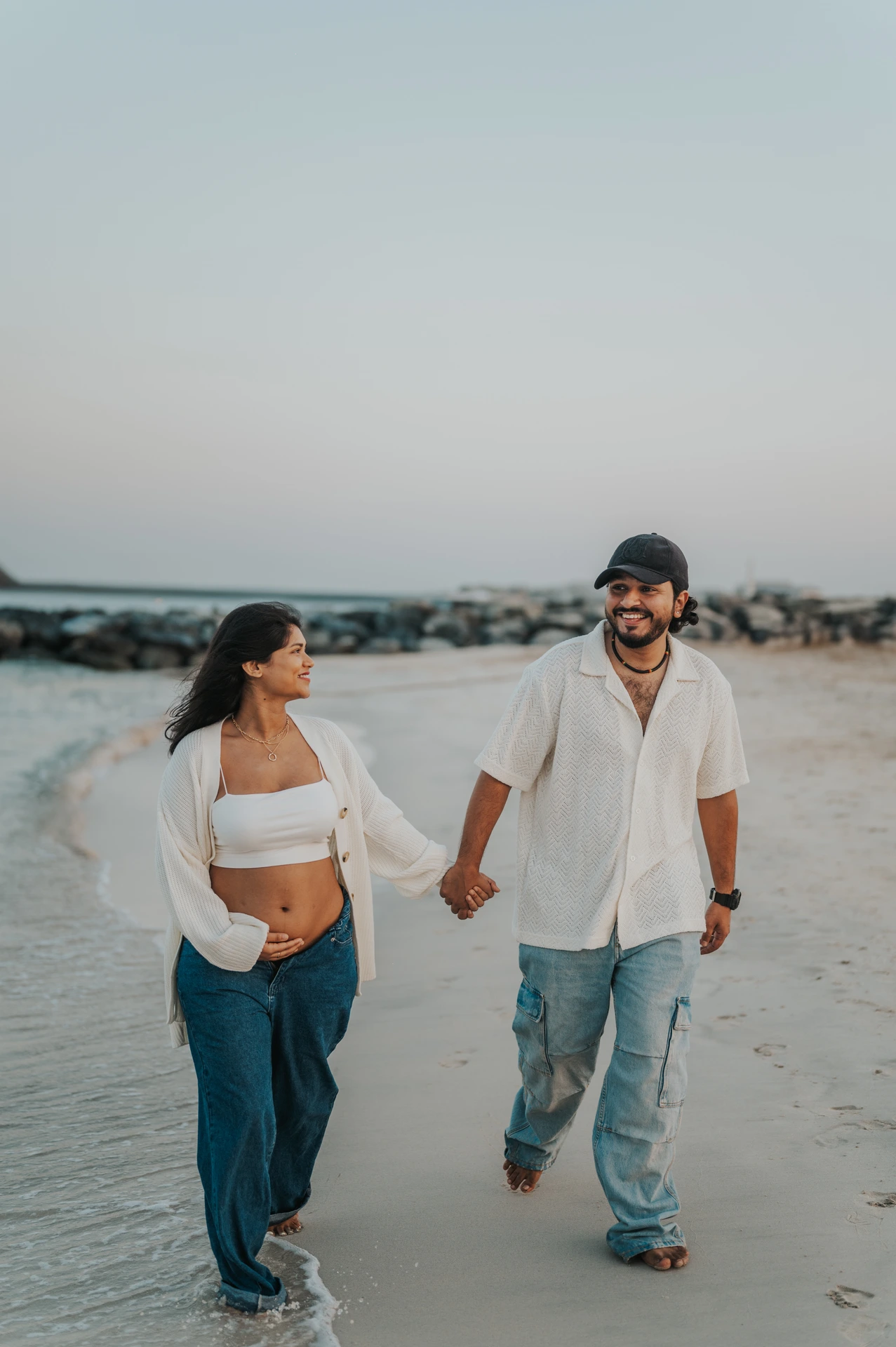 A couple walks along the shoreline in Dubai during a maternity photoshoot, creating relaxed movement and natural connection in the frame.