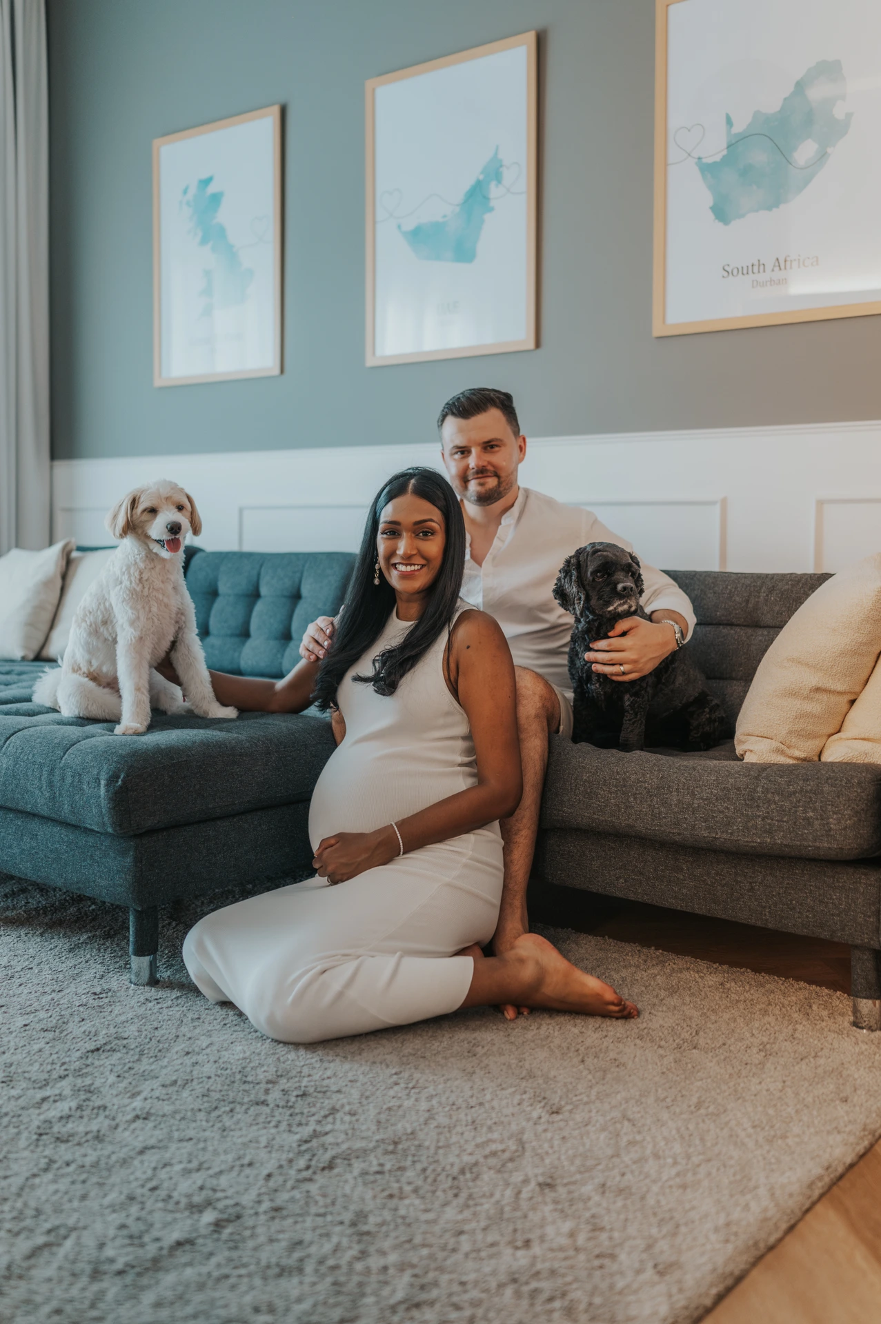 A pregnant couple poses with two dogs in their Dubai living room during a maternity photoshoot with pets, giving a relaxed at-home family feel.