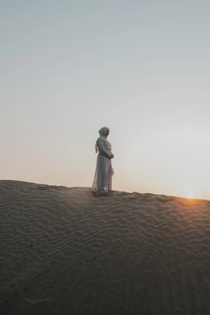 Maternity Photoshoot Dubai - mother on sunset dune An expecting mother stands on a Dubai desert dune during a maternity photoshoot, framed by rippled sand and soft evening light.