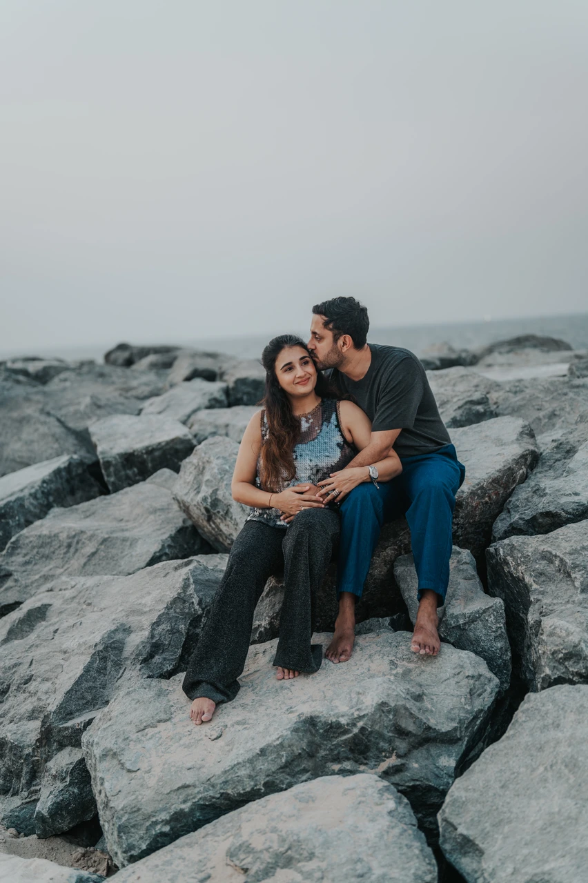 Maternity Photoshoot Dubai - wide rock portrait An expecting couple sits together on large coastal rocks in Dubai during a maternity photoshoot, creating a relaxed wide portrait by the sea.