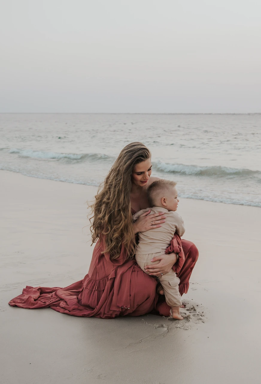 Maternity Photoshoot Dubai - beach cuddle with toddler A mother cuddles her toddler on Dubai beach during a maternity and family photoshoot, captured near the shoreline with calm evening tones.