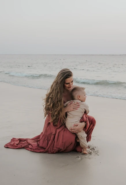 Maternity Photoshoot Dubai - beach cuddle with toddler A mother cuddles her toddler on Dubai beach during a maternity and family photoshoot, captured near the shoreline with calm evening tones.
