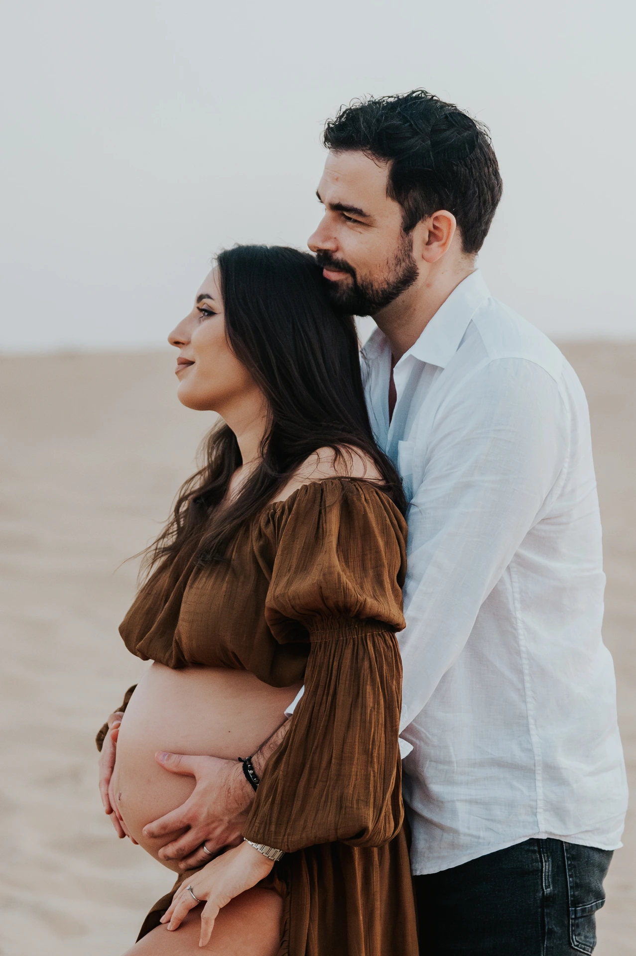 Sunrise vs sunset Dubai maternity photoshoot - intimate sunset couple profile A maternity couple stands in a close side-profile portrait during a maternity photoshoot in Dubai, with warm sunset tones and elegant framing.