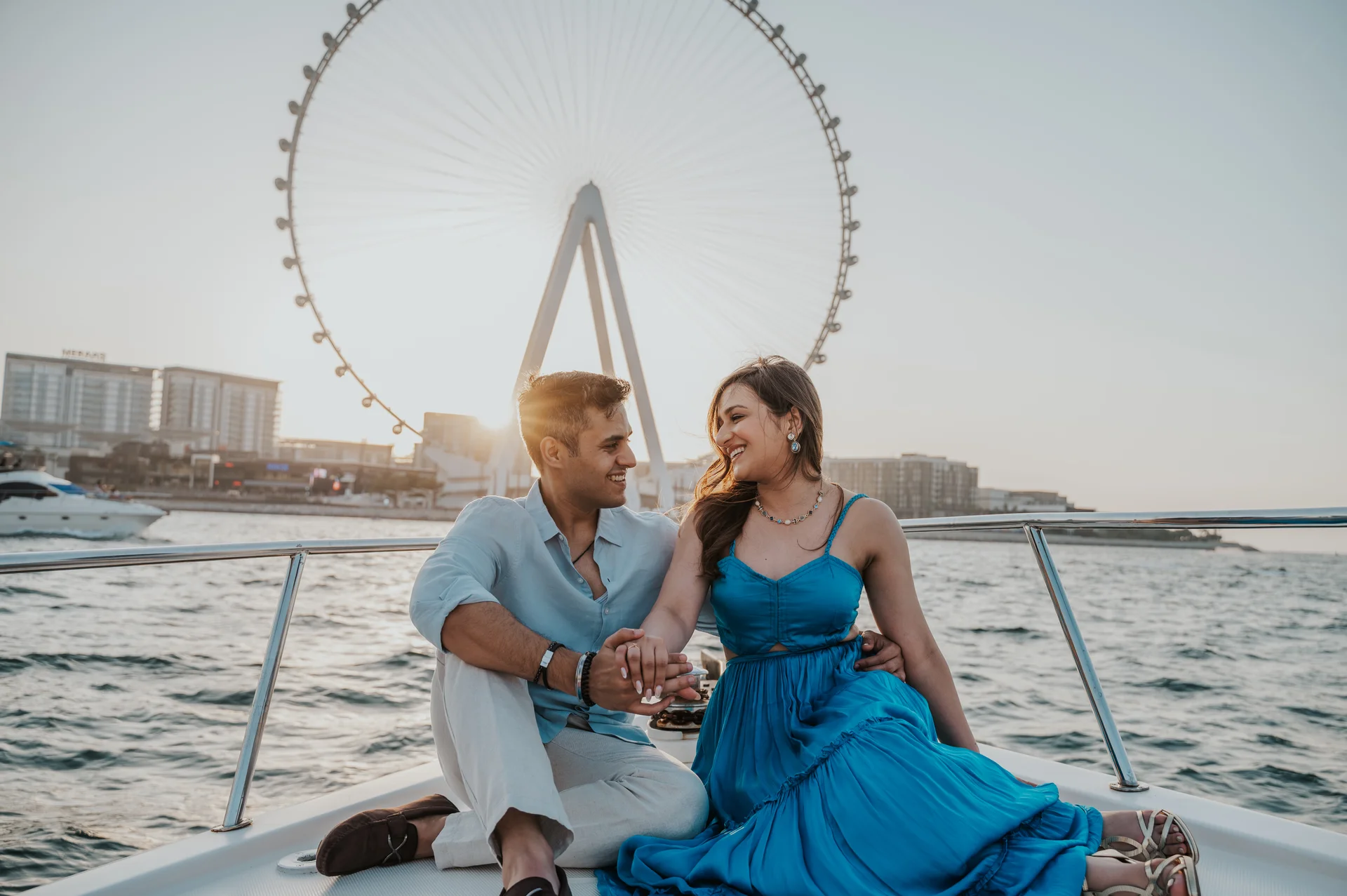 Ain Dubai Proposal Yacht Portrait A couple sits hand in hand on a yacht with Ain Dubai behind them during a relaxed Dubai proposal photography portrait.