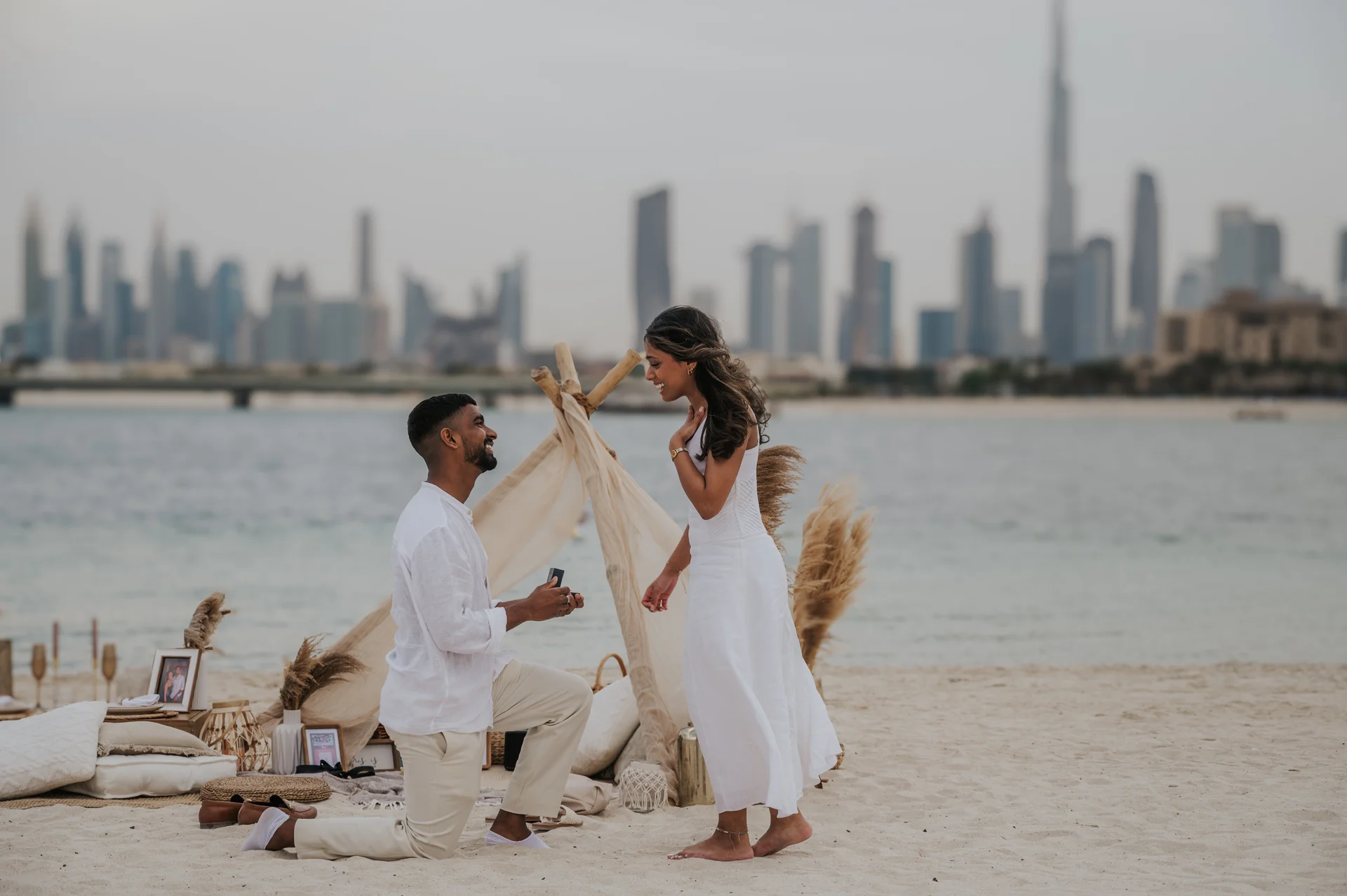 Proposing at a Burj Khalifa Beach Picnic A man kneels with an open ring box beside a beach picnic with Burj Khalifa behind their Dubai proposal.