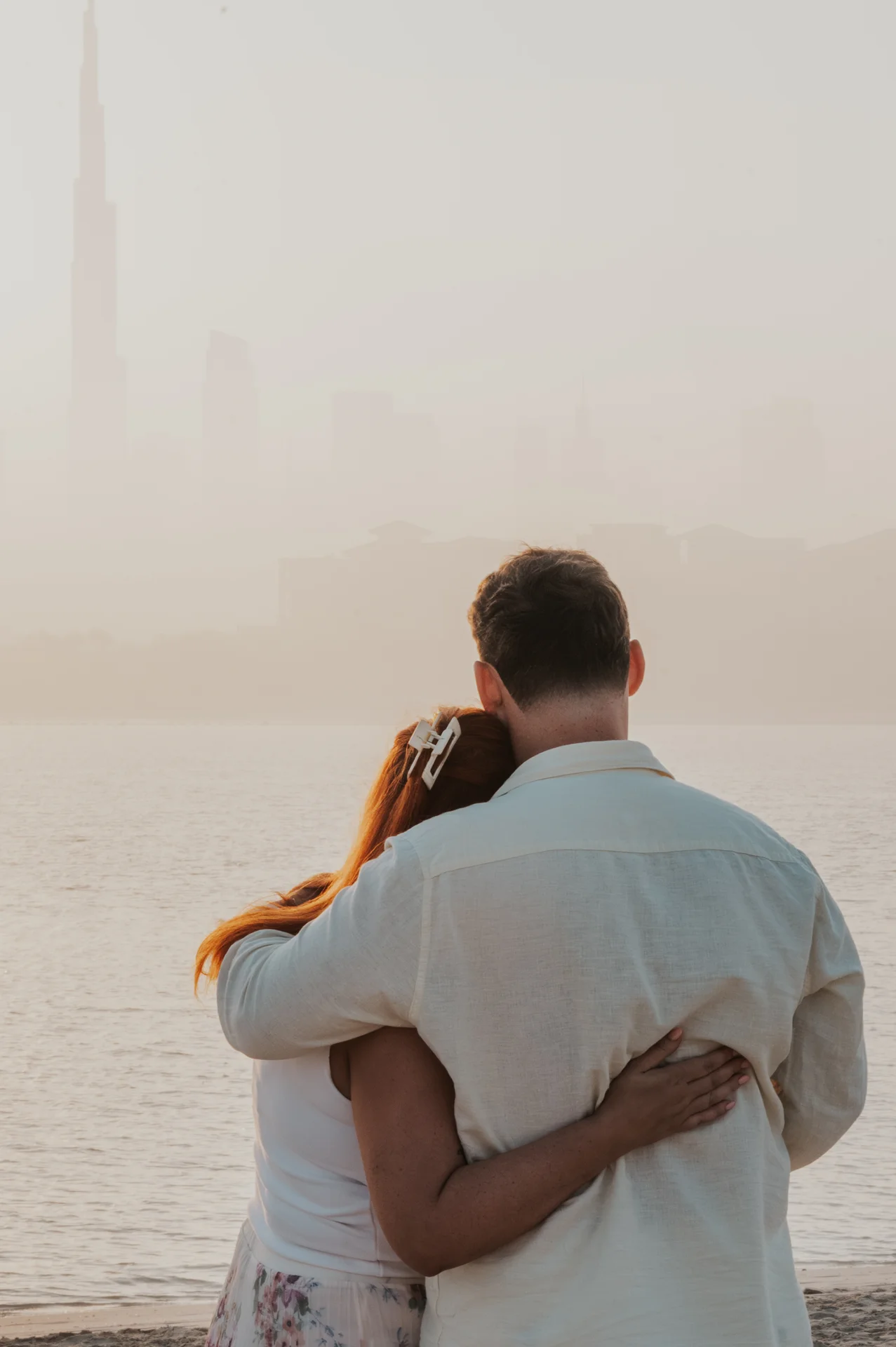 Dubai Proposal Embrace at Golden Hour A couple embraces beside the water at golden hour with Dubai’s hazy skyline behind their proposal photography portrait.