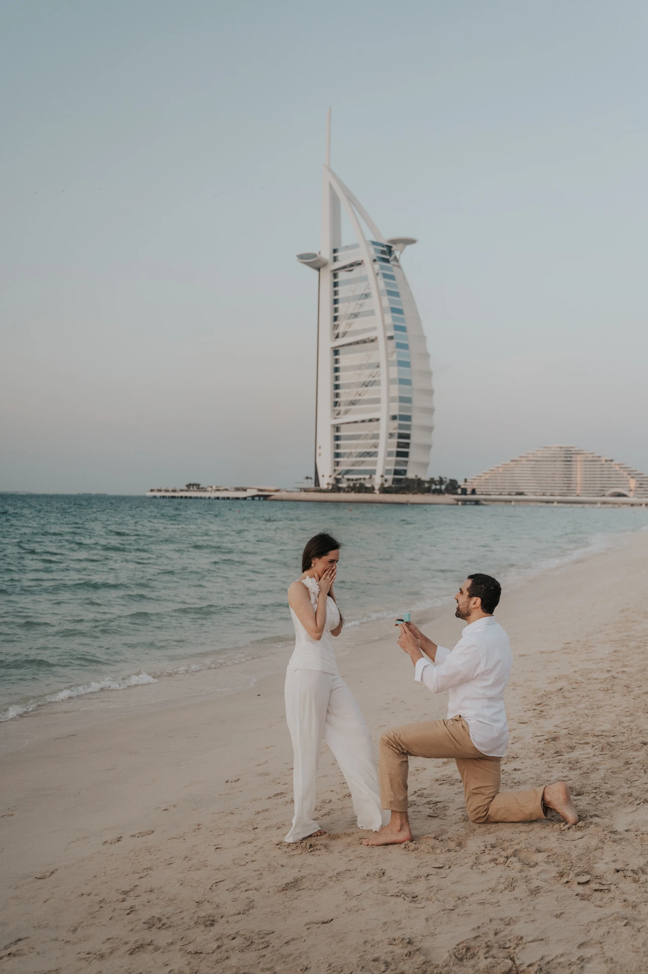 Burj Al Arab Beach Proposal in Dubai A man kneels with an open turquoise ring box on the beach below Burj Al Arab during a Dubai proposal.