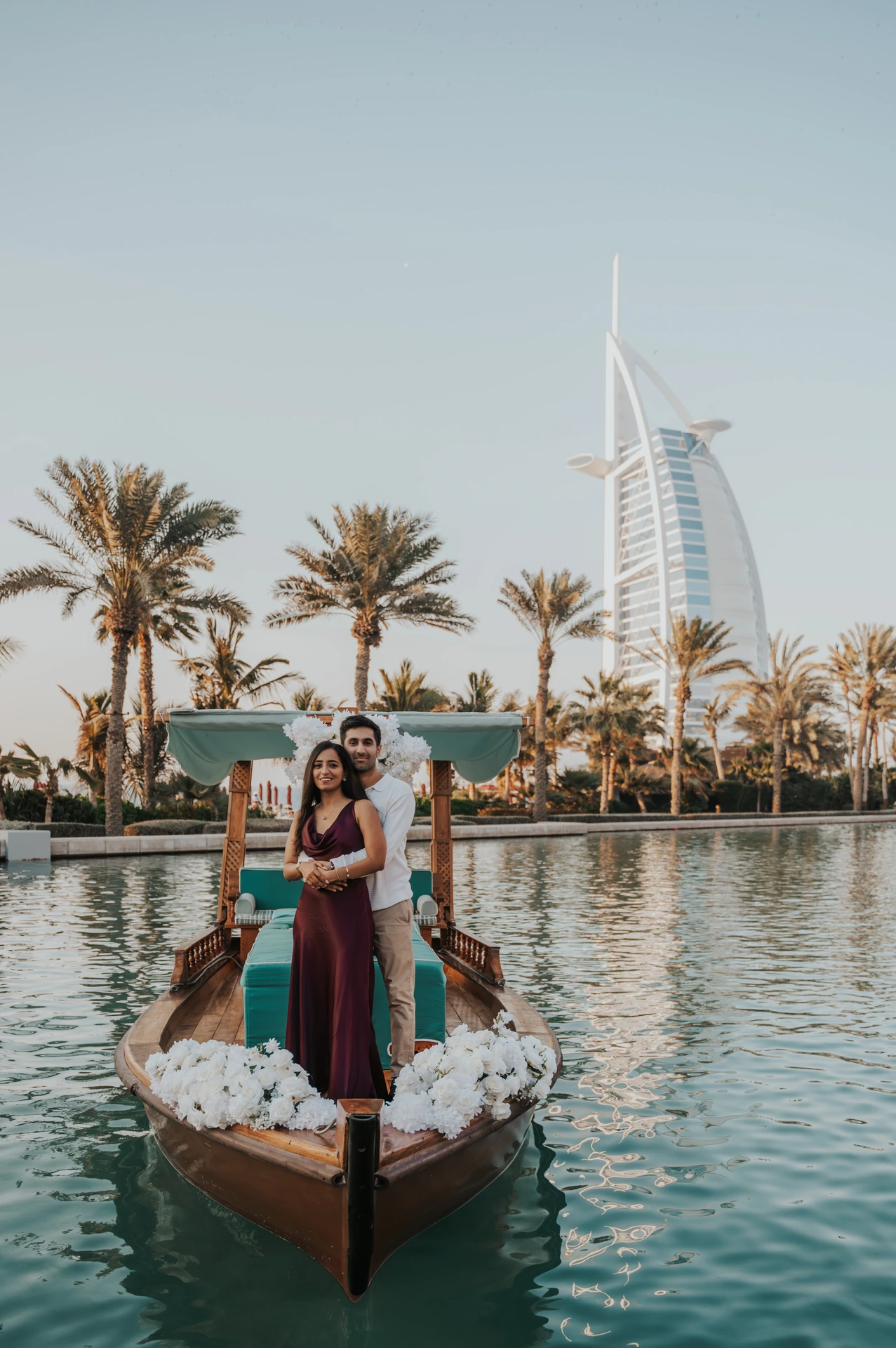 A couple stands on a decorated abra near Shimmers in Dubai during proposal planning, with palms and calm waterfront reflections around them.