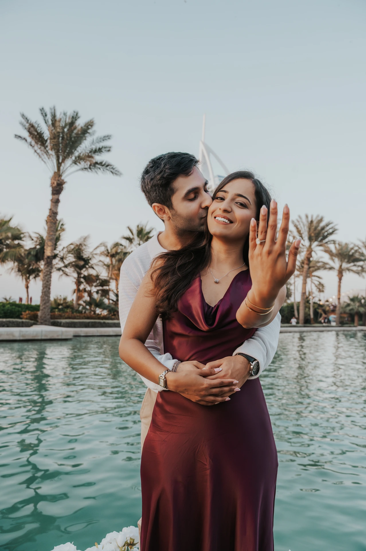 A couple embraces near Shimmers in Dubai and showcases the engagement ring after the proposal, framed with palm-lined waterfront scenery.