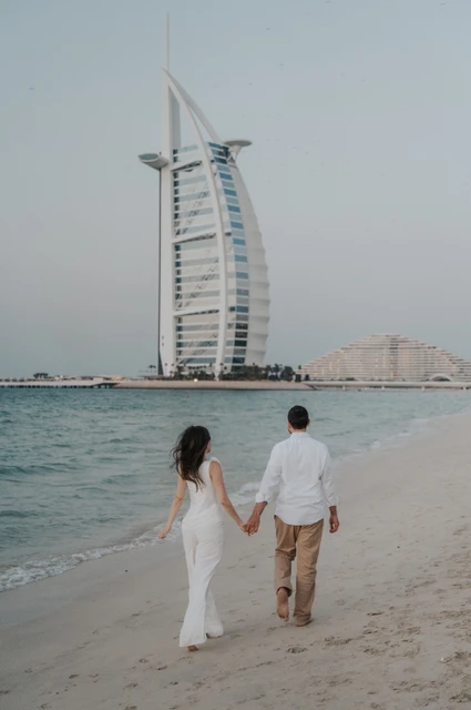 A couple walks along the waterline near Shimmers in Dubai after a proposal, with Burj Al Arab clearly visible in the frame.