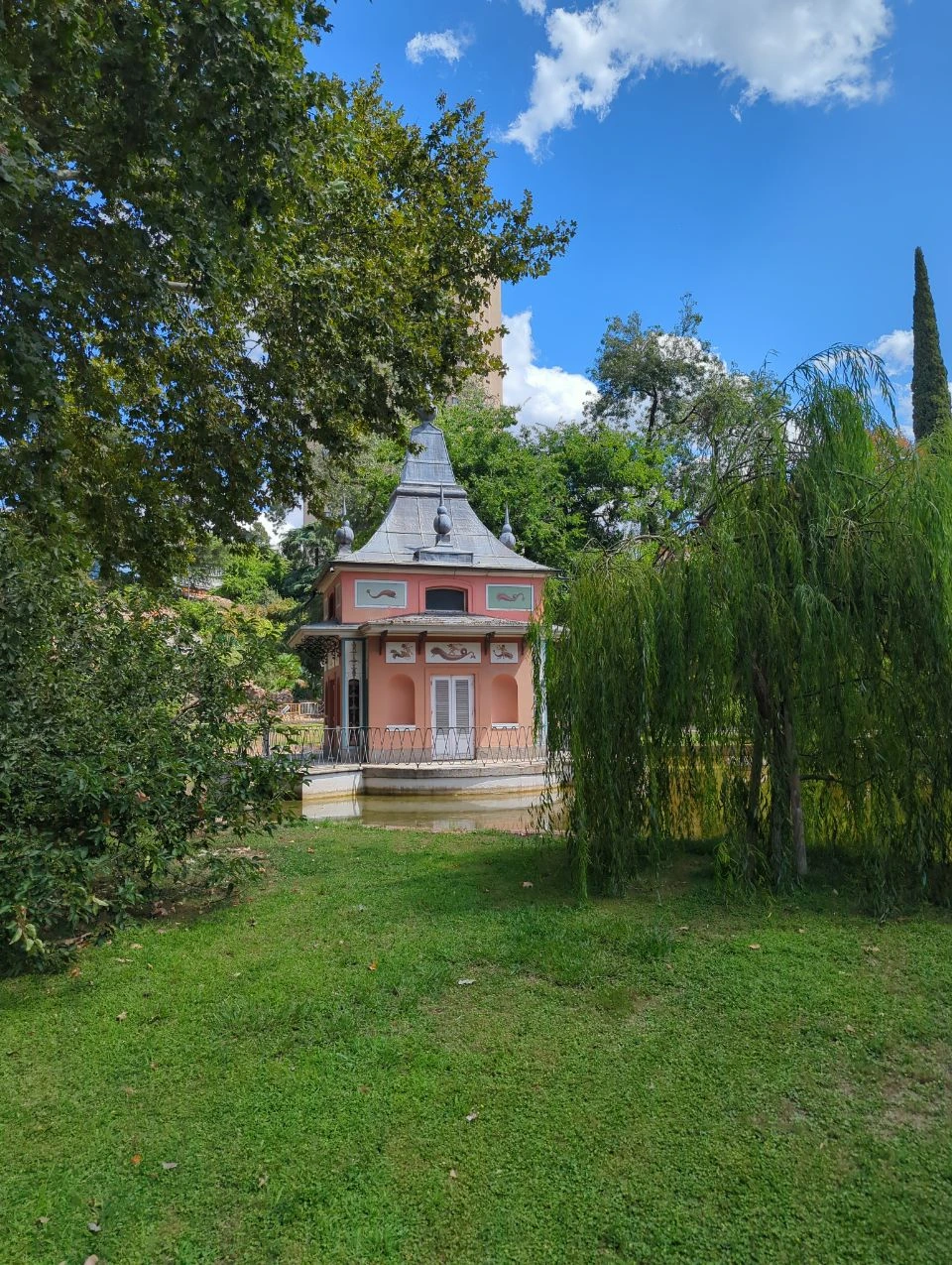 El Retiro Photoshoot Route - Pink Garden Pavilion A pink garden pavilion stands between trees and lawn in El Retiro, showing a playful final stop on the Madrid photoshoot route.