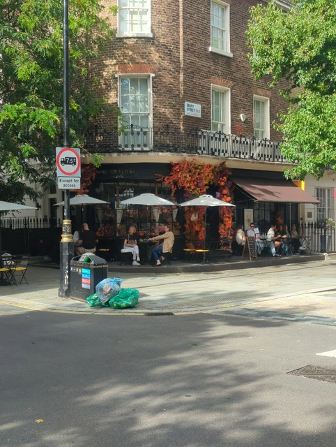 Tomtom Coffee House with a dark frontage, orange floral decoration and outdoor tables beside the Ebury Street sign