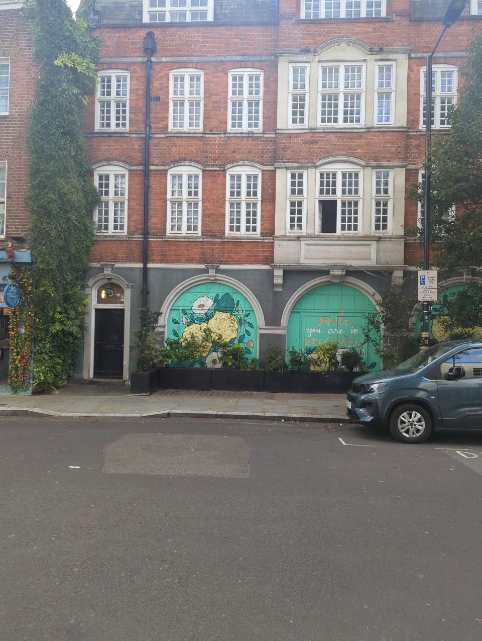 Turquoise window panels with illustrated flowers and Smile you are in Belgravia lettering beneath red-brick upper floors