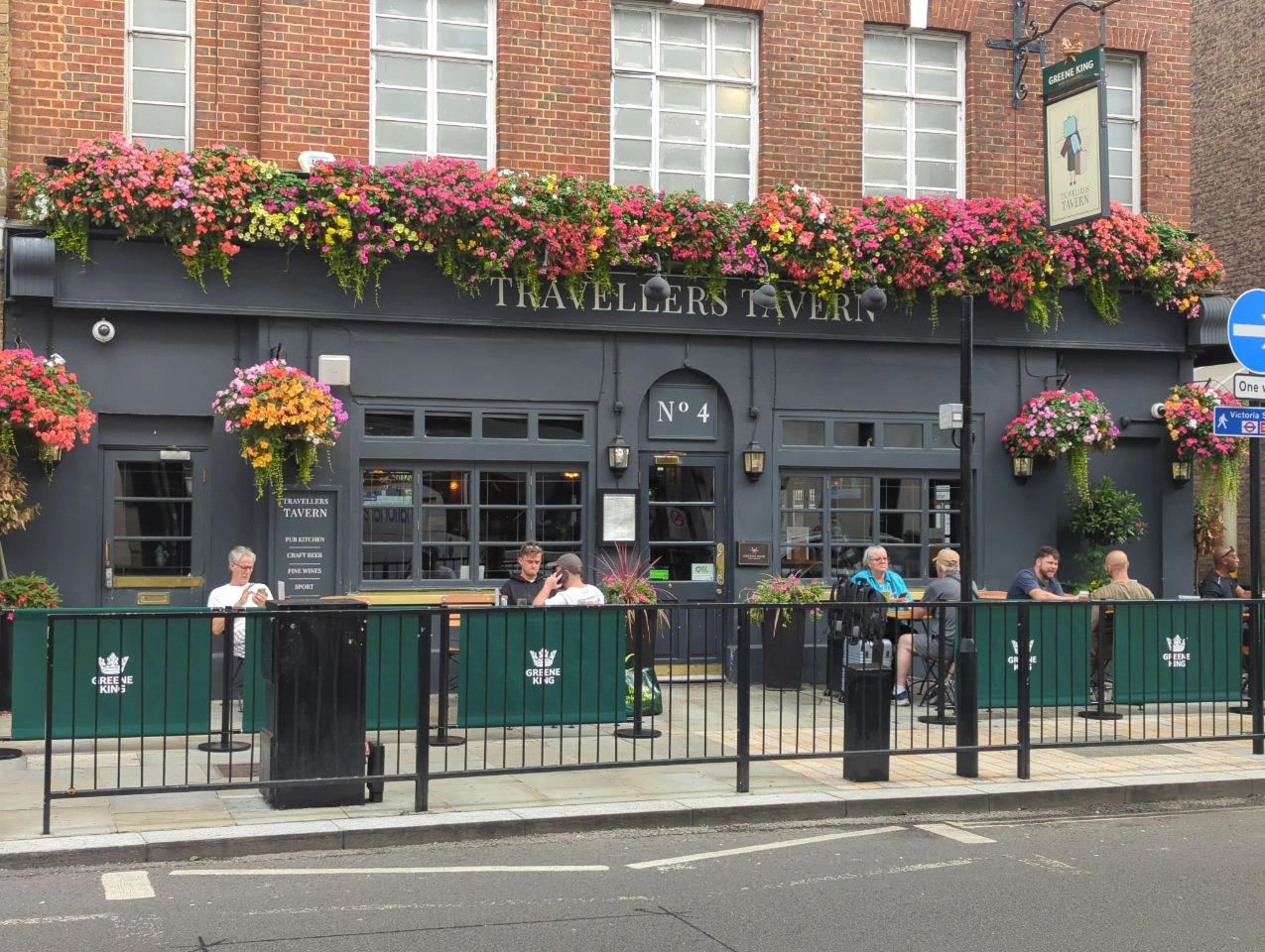 Dark grey Travellers Tavern frontage with number four above the door, bright hanging baskets and outdoor diners