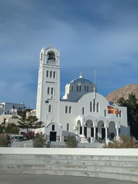 White church and bell tower in an open square in Emporio, Santorini