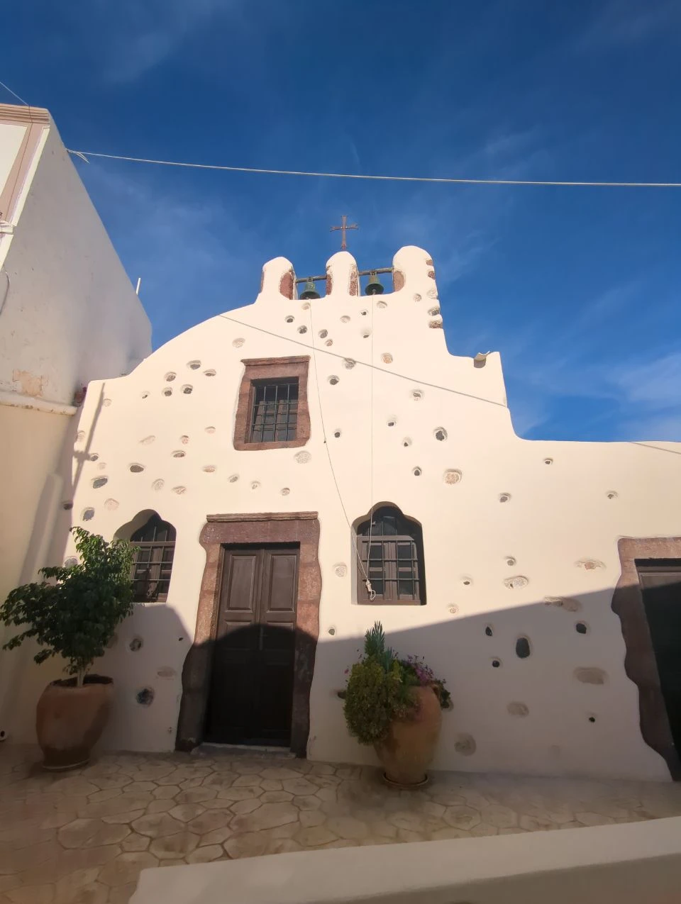 Emporio textured church facade | Santorini White Emporio church facade with dark wooden doorway, small windows and rough stone details