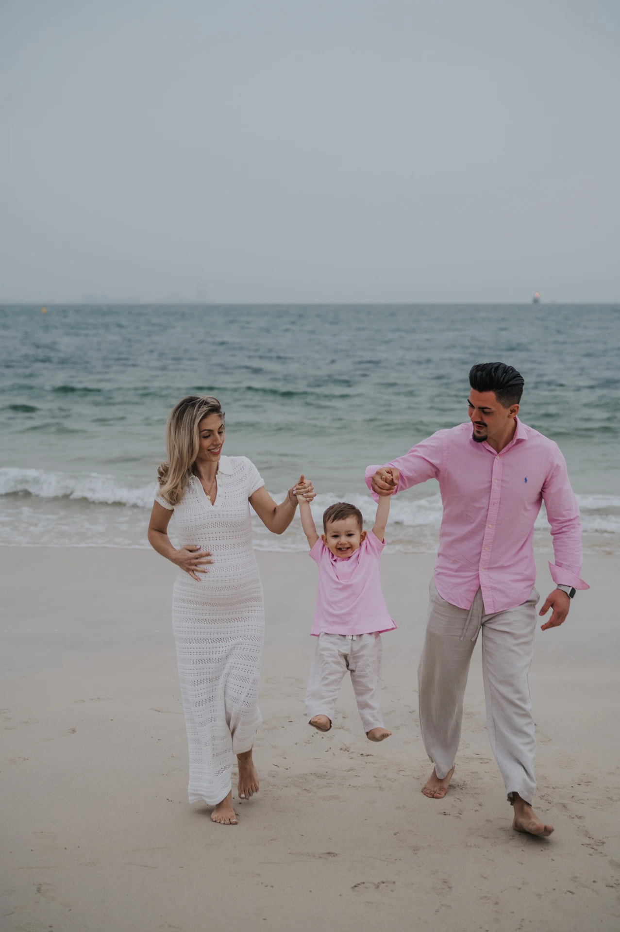 Parents lift and spin their child on Dubai beach while walking together during a playful family beach photoshoot.