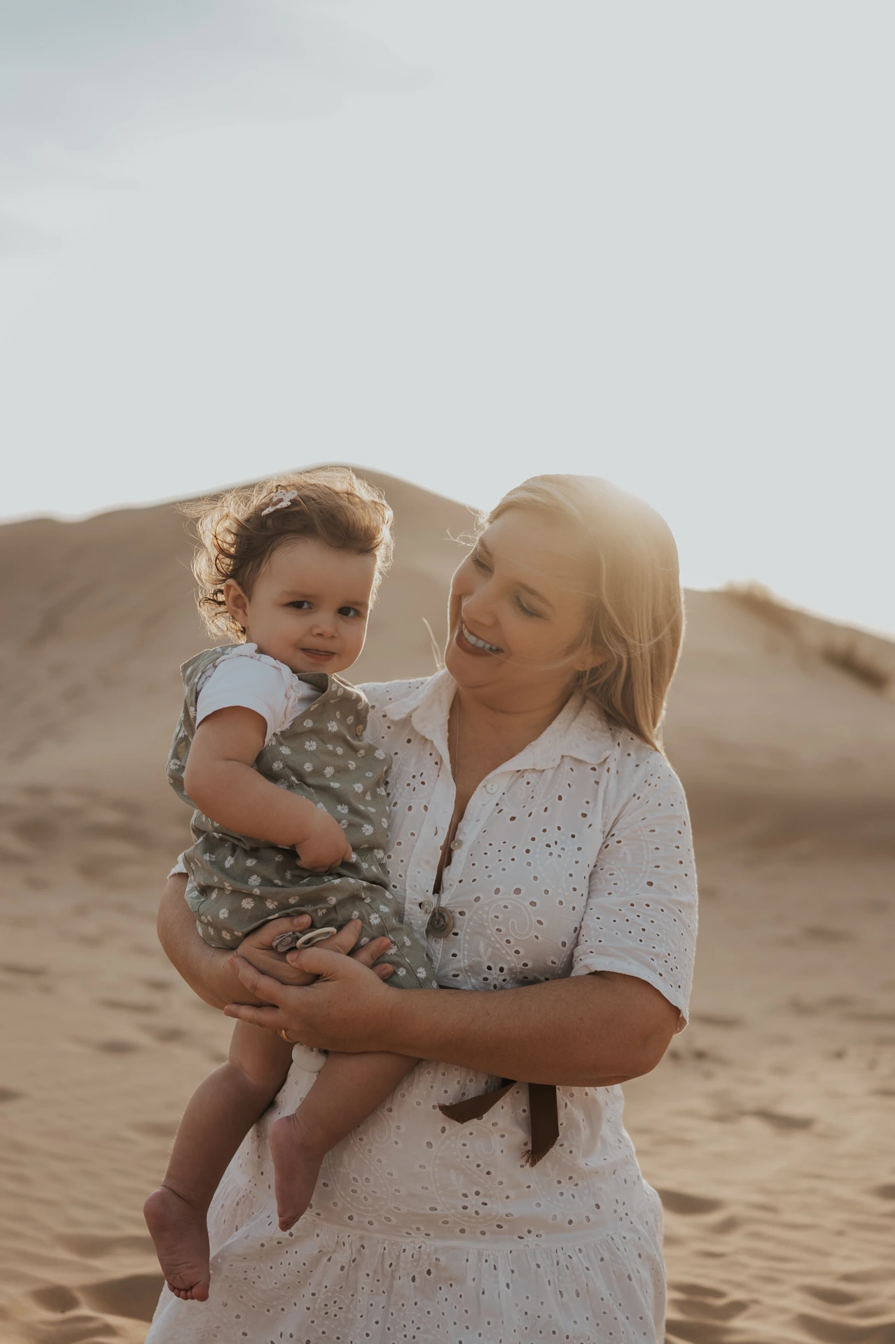 Mother holding her toddler on sandy dunes at sunset in Dubai, capturing a warm, candid family session moment.