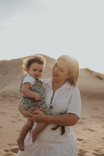 Family photoshoot in Dubai Mother holding her toddler on sandy dunes at sunset in Dubai, capturing a warm, candid family session moment.