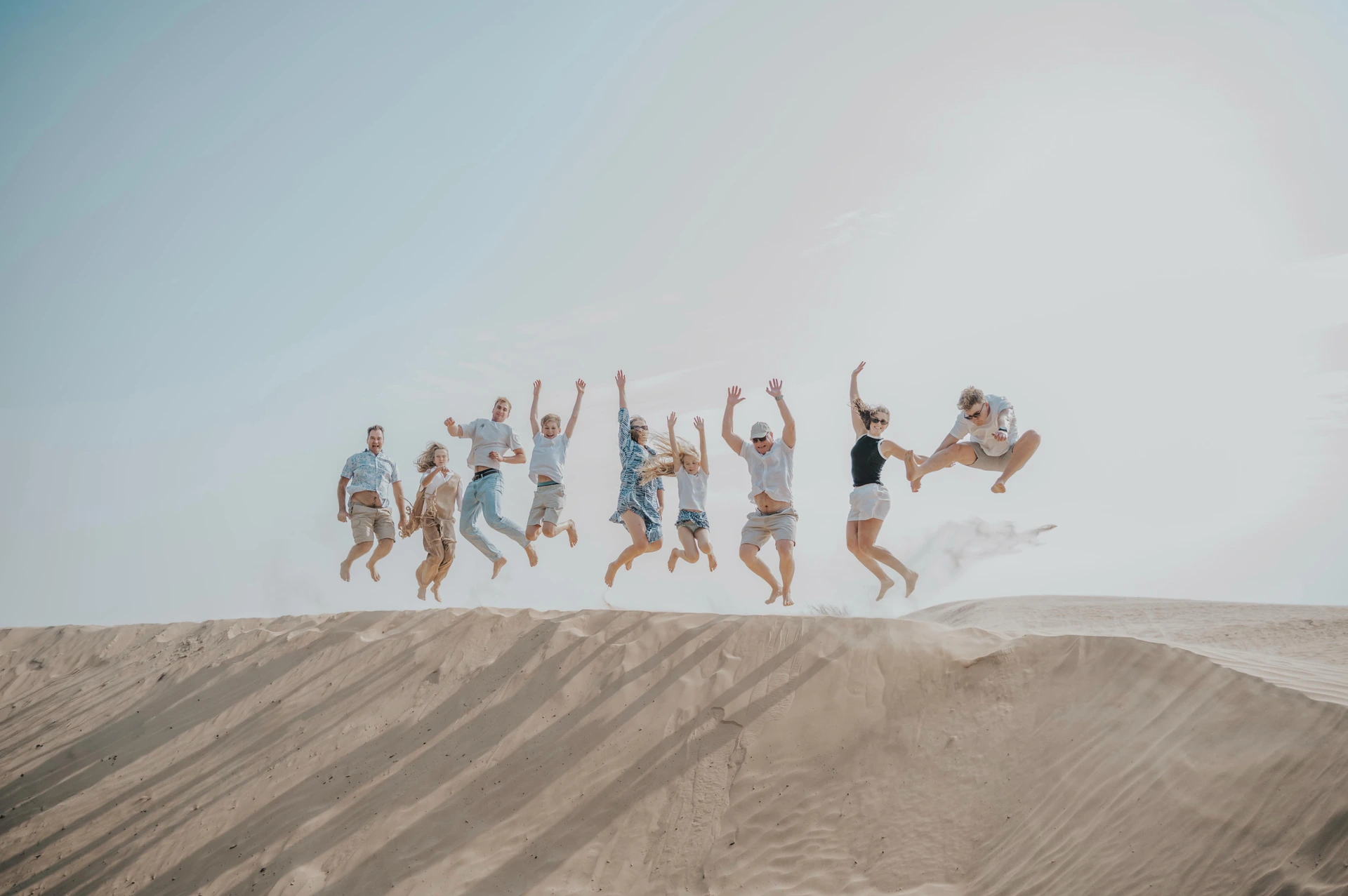 A large family jumps together on a sandy dune in Dubai during a playful family session.