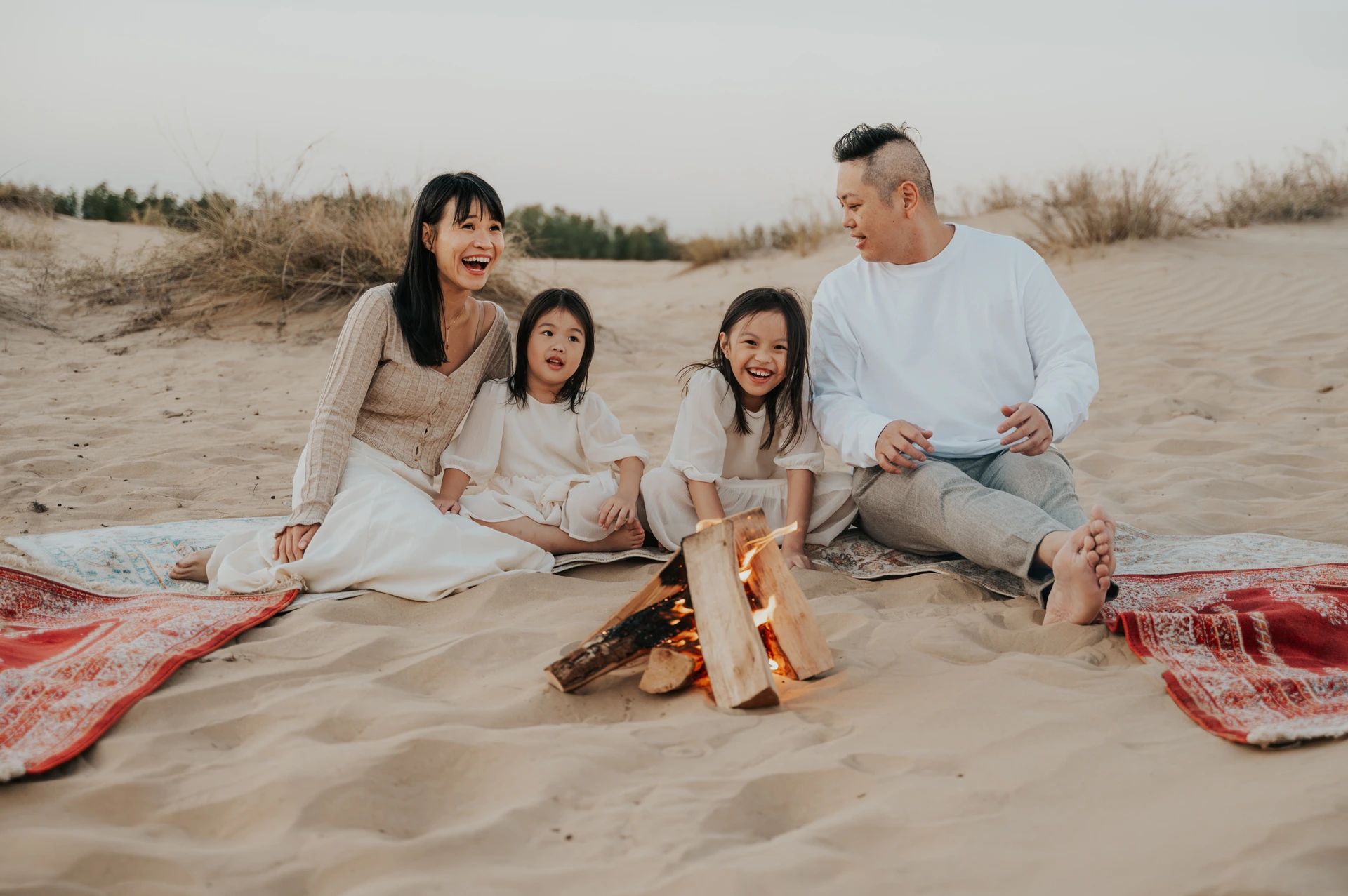 Family of four smiling beside a small campfire on desert blankets during a Dubai family photoshoot at sunset.