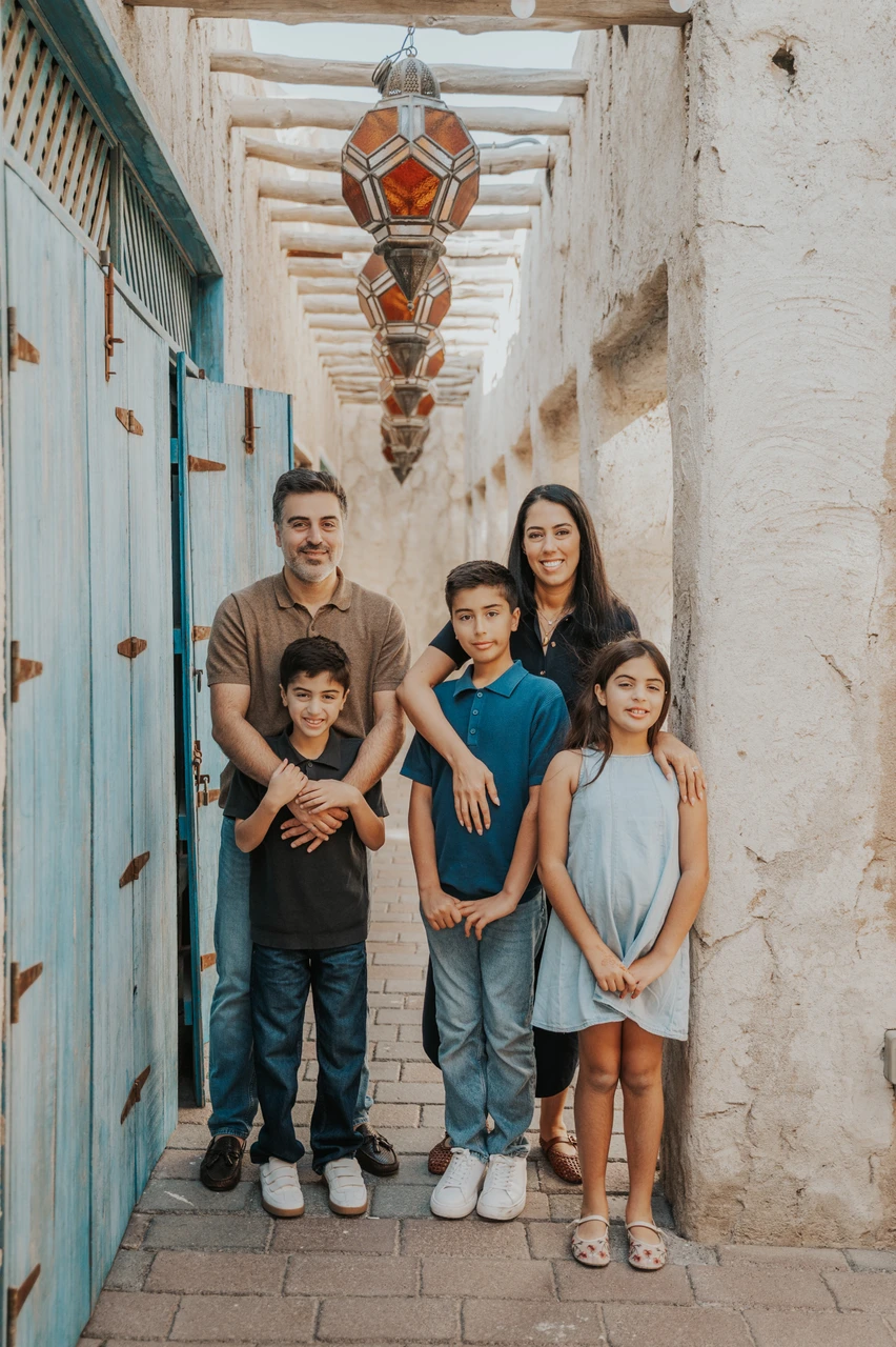 Family photoshoot in Old Dubai - parents with three kids Parents stand with their three children in an Old Dubai alley during a classic family photoshoot portrait.