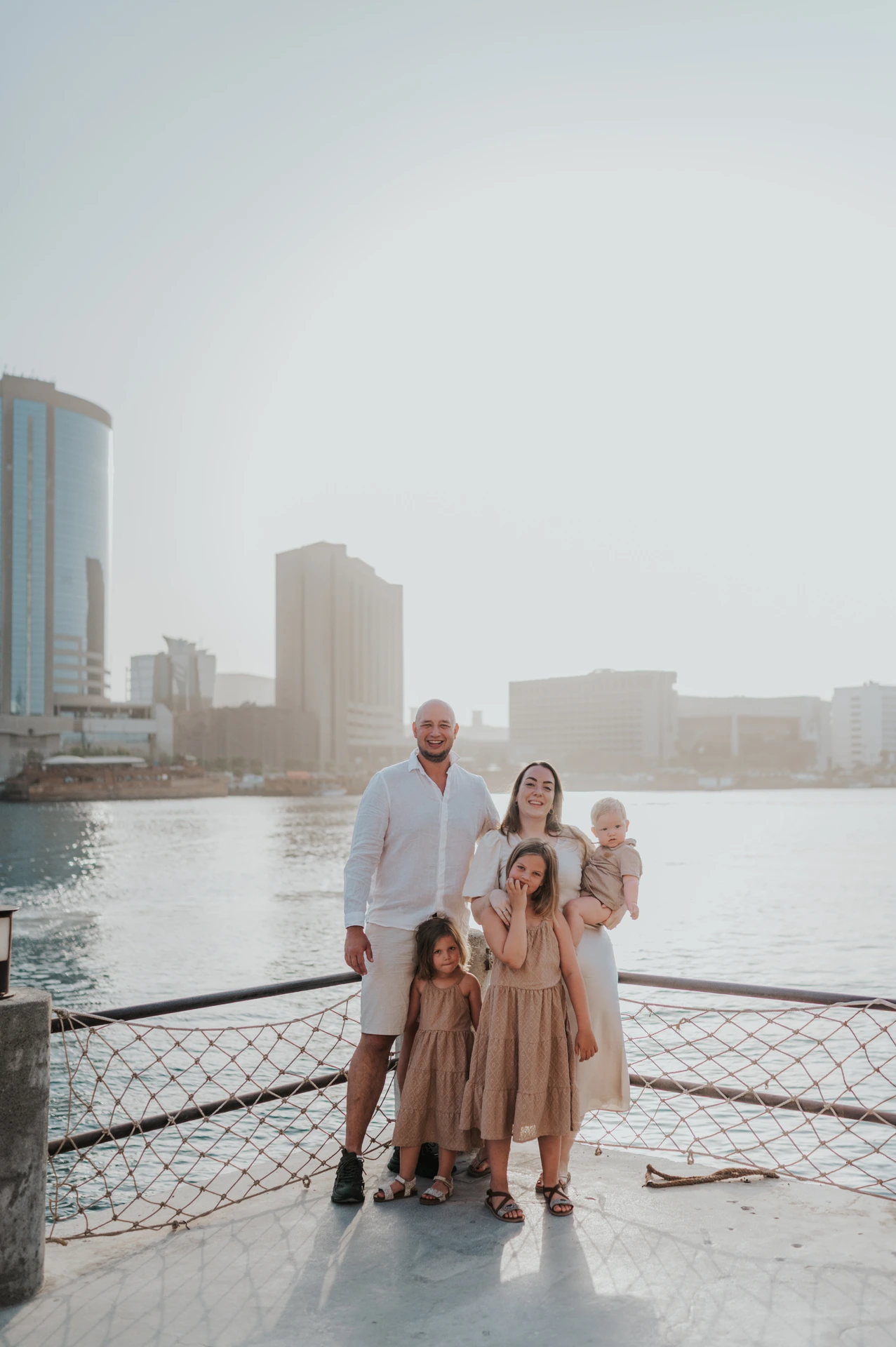 A family stands by Dubai Creek with city skyline in the background during an Old Dubai family photoshoot.