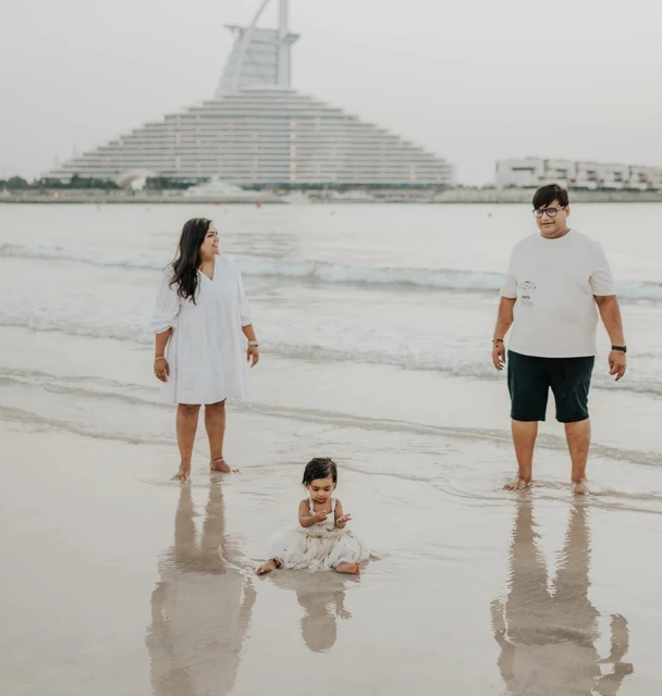 Parents stand at the shoreline while their toddler plays in shallow water on Dubai beach during a natural family photoshoot session.