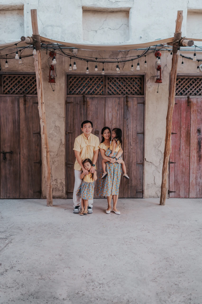Family photoshoot in Dubai - old town family portrait A family with two toddlers stands in front of traditional wooden doors in Old Dubai during a family photoshoot.