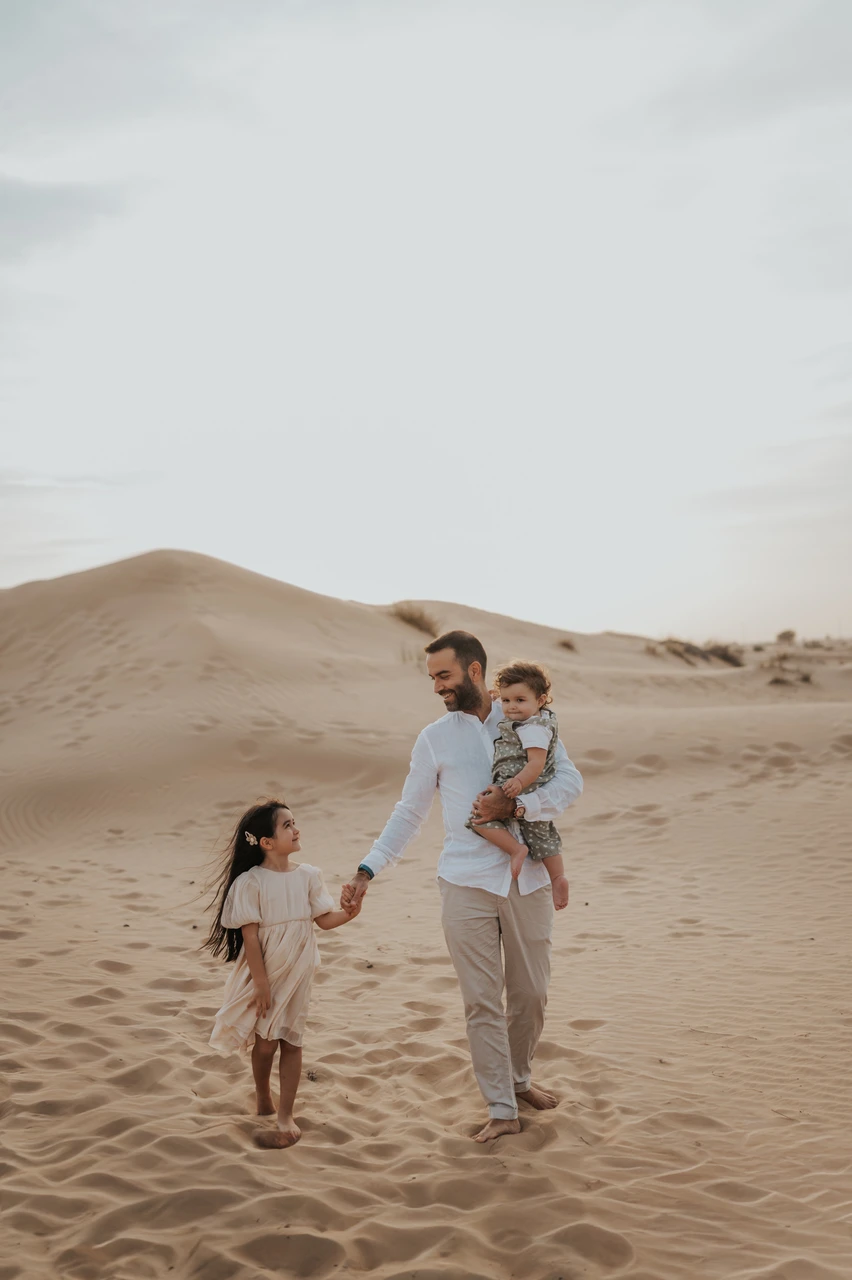 Family photoshoot in Dubai - desert family adventure Parents and toddler move through Dubai desert dunes during golden hour in a scenic family photoshoot moment.