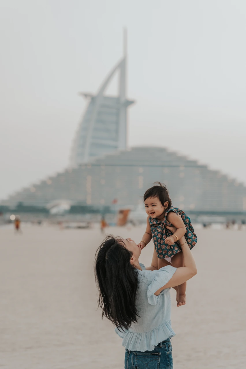 Family photoshoot in Dubai - toddler shoulder close-up A toddler sits on a parent’s shoulder on Dubai beach with Burj Al Arab blurred behind during a family photoshoot.