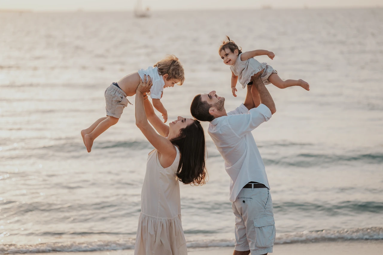 Family photoshoot in Dubai - parents lifting toddlers Parents lift their toddlers in the air by the Dubai shoreline during a joyful golden-hour family photoshoot.