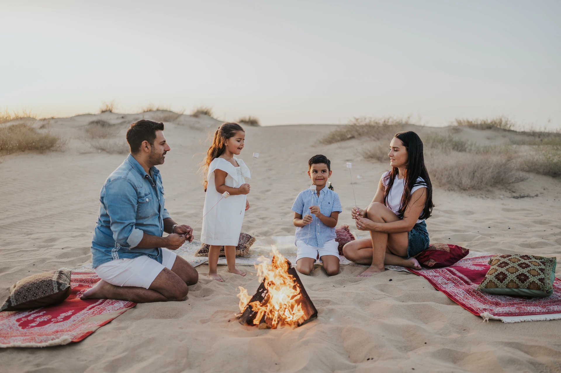 Family of four around a small campfire on desert rugs in Dubai, relaxed moments for a family photoshoot.