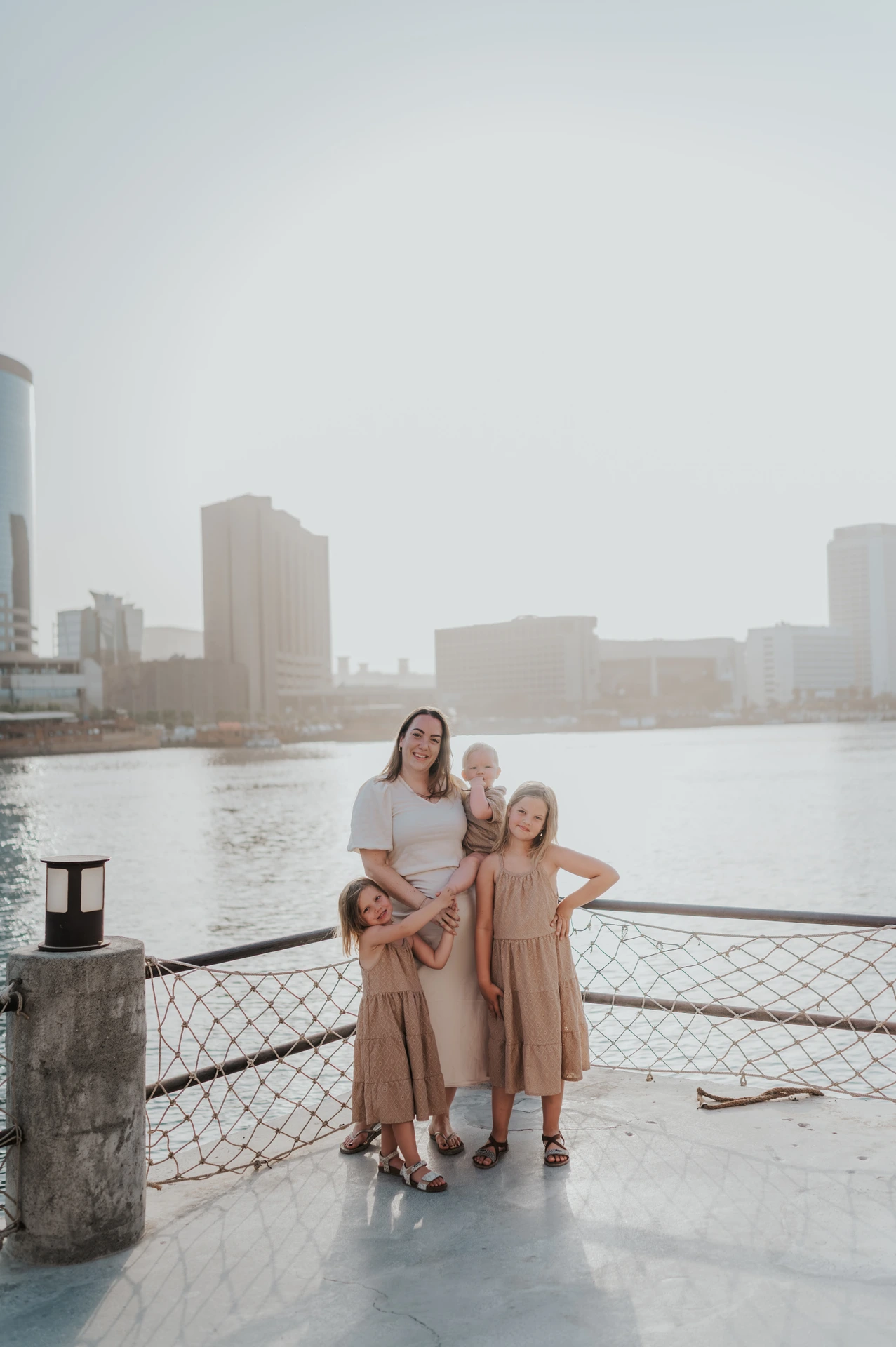 Mother with three children posing by Dubai Creek railing at sunset during a relaxed family photoshoot.