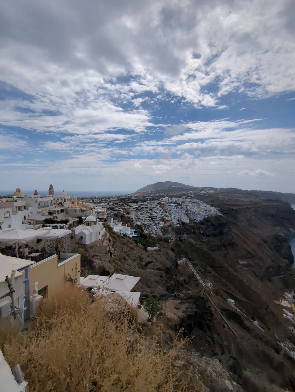 Fira caldera panorama | Best views in Santorini White Fira rooftops and churches along Santorini's caldera rim beneath a broad cloudy sky
