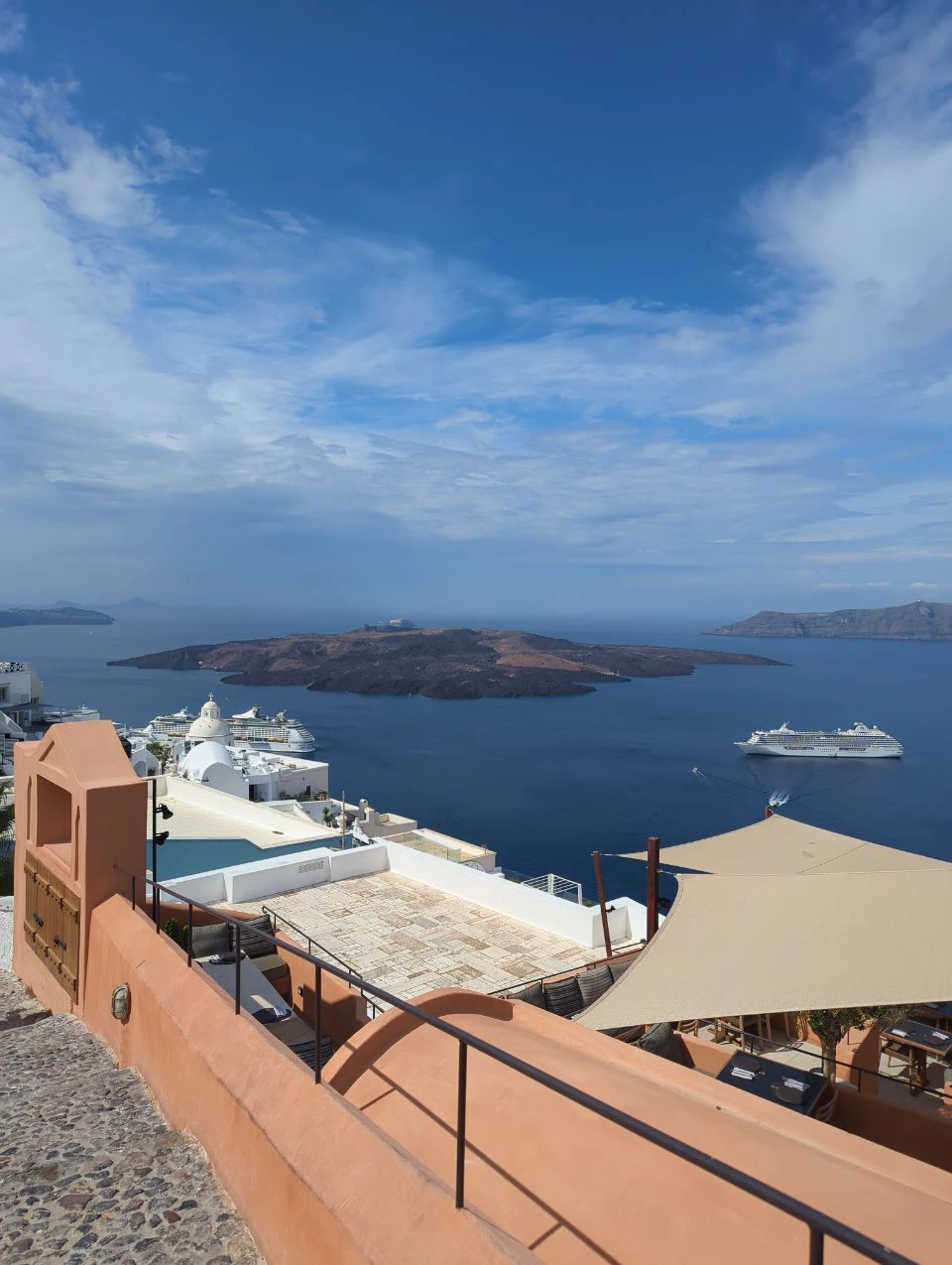 Orange steps on Fira caldera walk | Santorini Orange stairway and black railing above Fira rooftops, with the Santorini caldera and cruise ships beyond