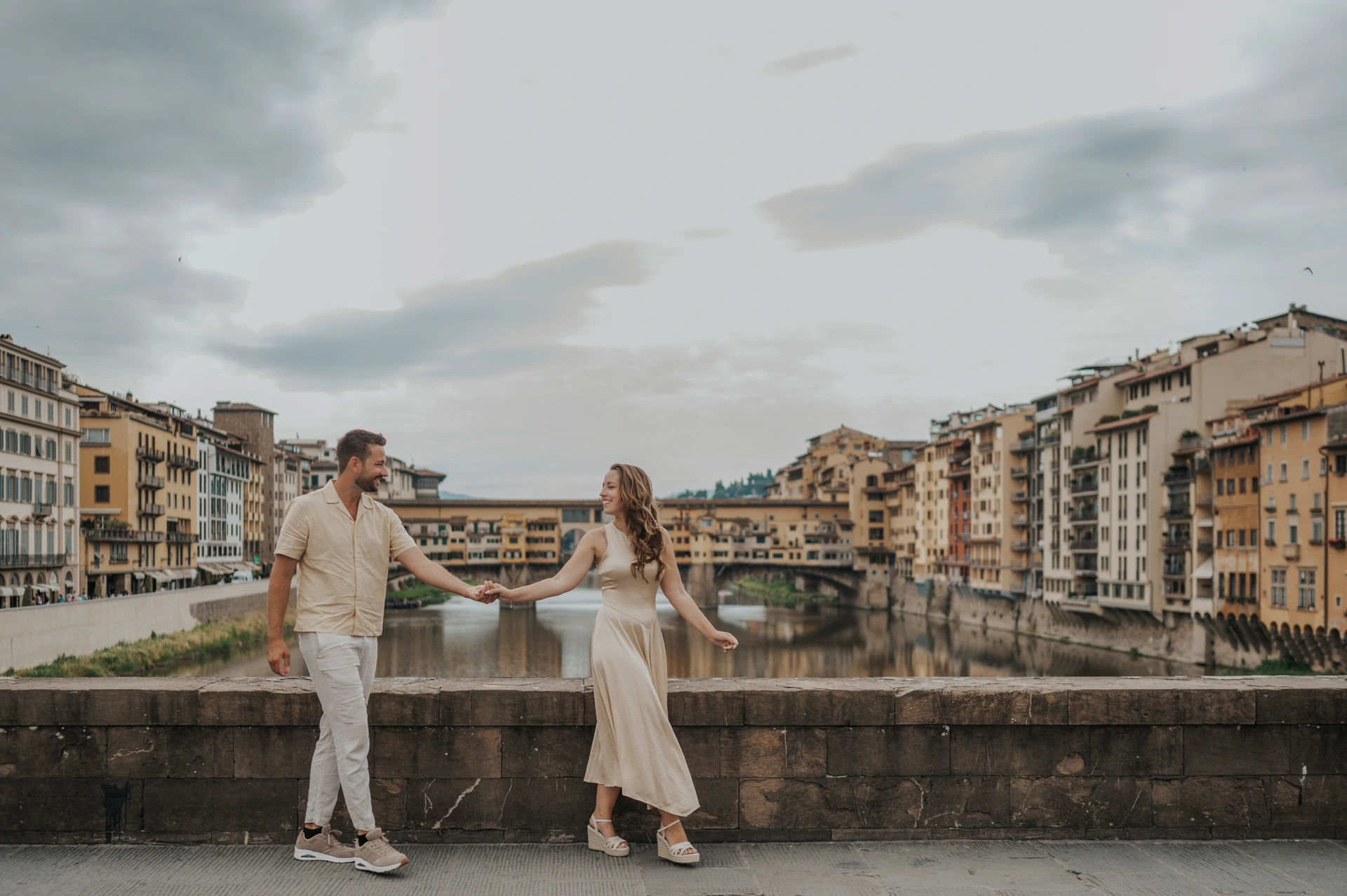 Una coppia si guarda tenendosi per mano lungo l’Arno, con Ponte Vecchio alle spalle.