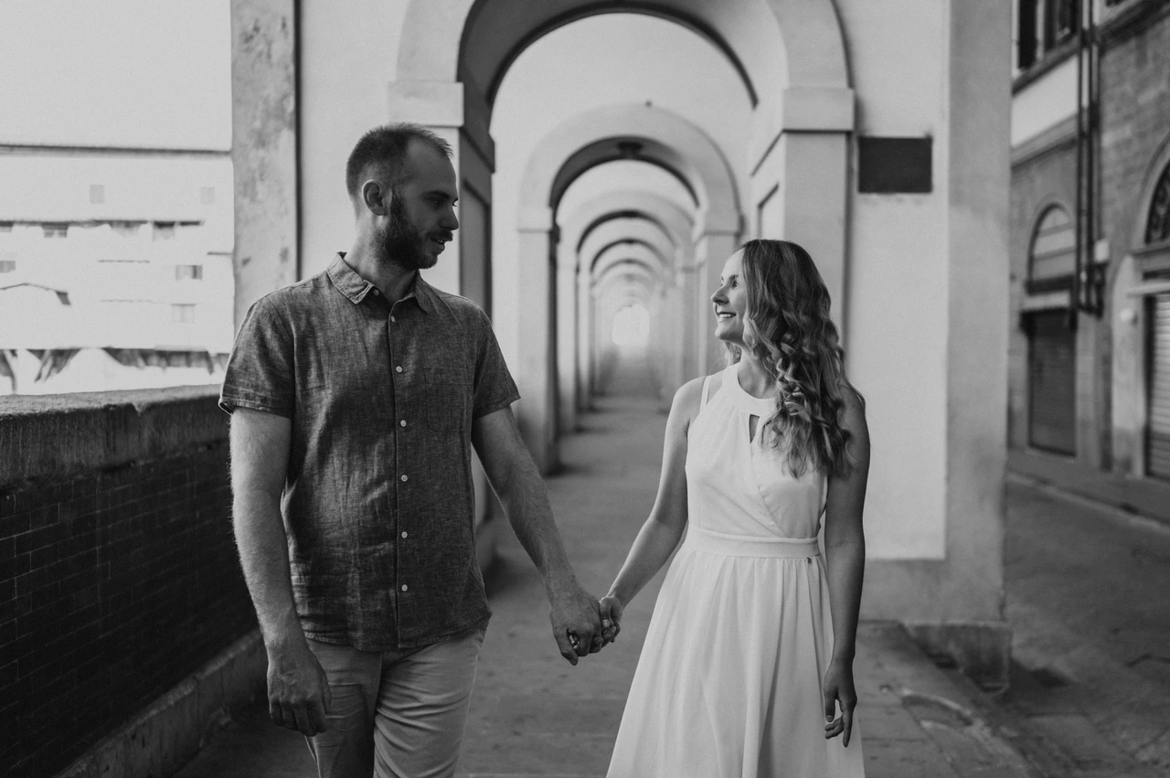 Florence couple photoshoot beneath the arches in black and white Black-and-white photograph of the couple walking through an arched passage during their Florence couple photoshoot.