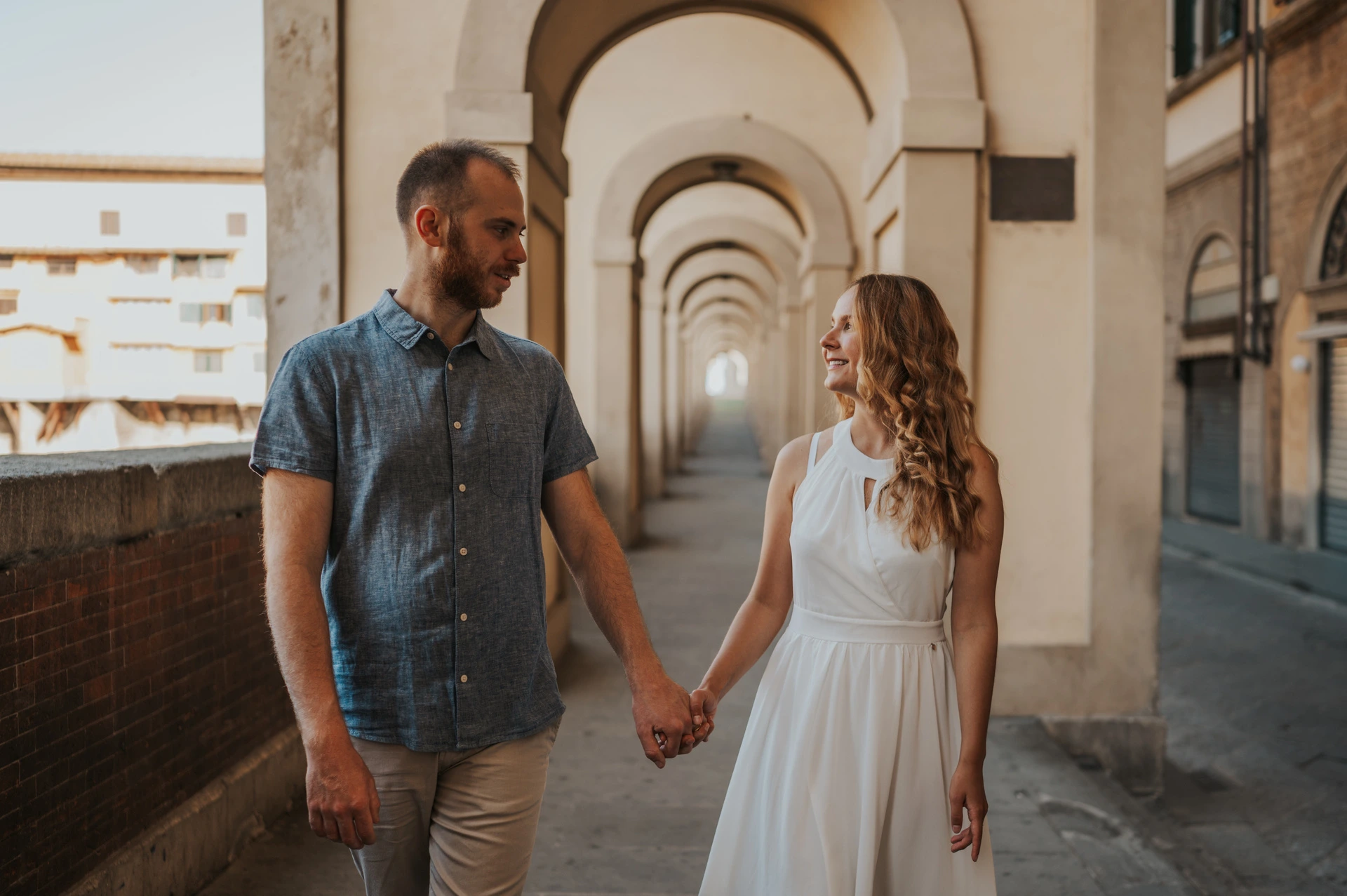 The couple walk beneath pale stone arches and look at each other during their Florence photoshoot.