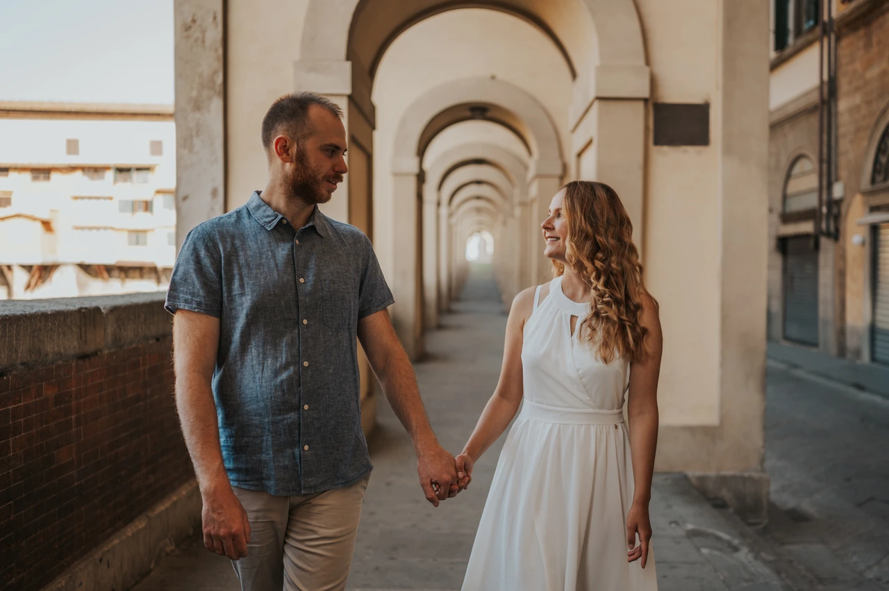 A walk beneath the arches during a Florence couple photoshoot The couple walk beneath pale stone arches and look at each other during their Florence photoshoot.