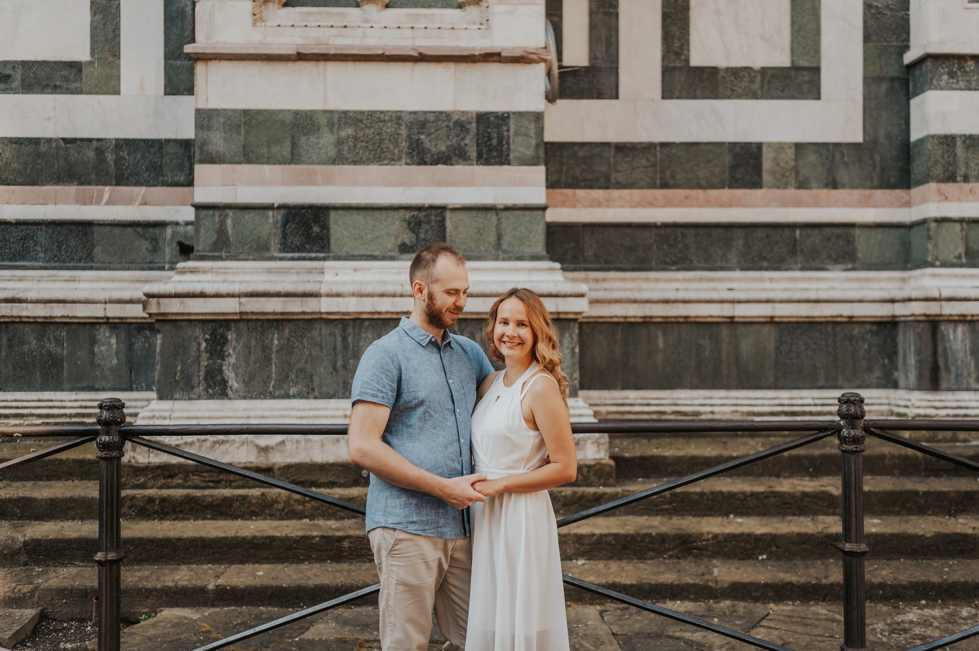 The couple smile together beside a railing with green and white marble behind them during their Florence couple photoshoot.