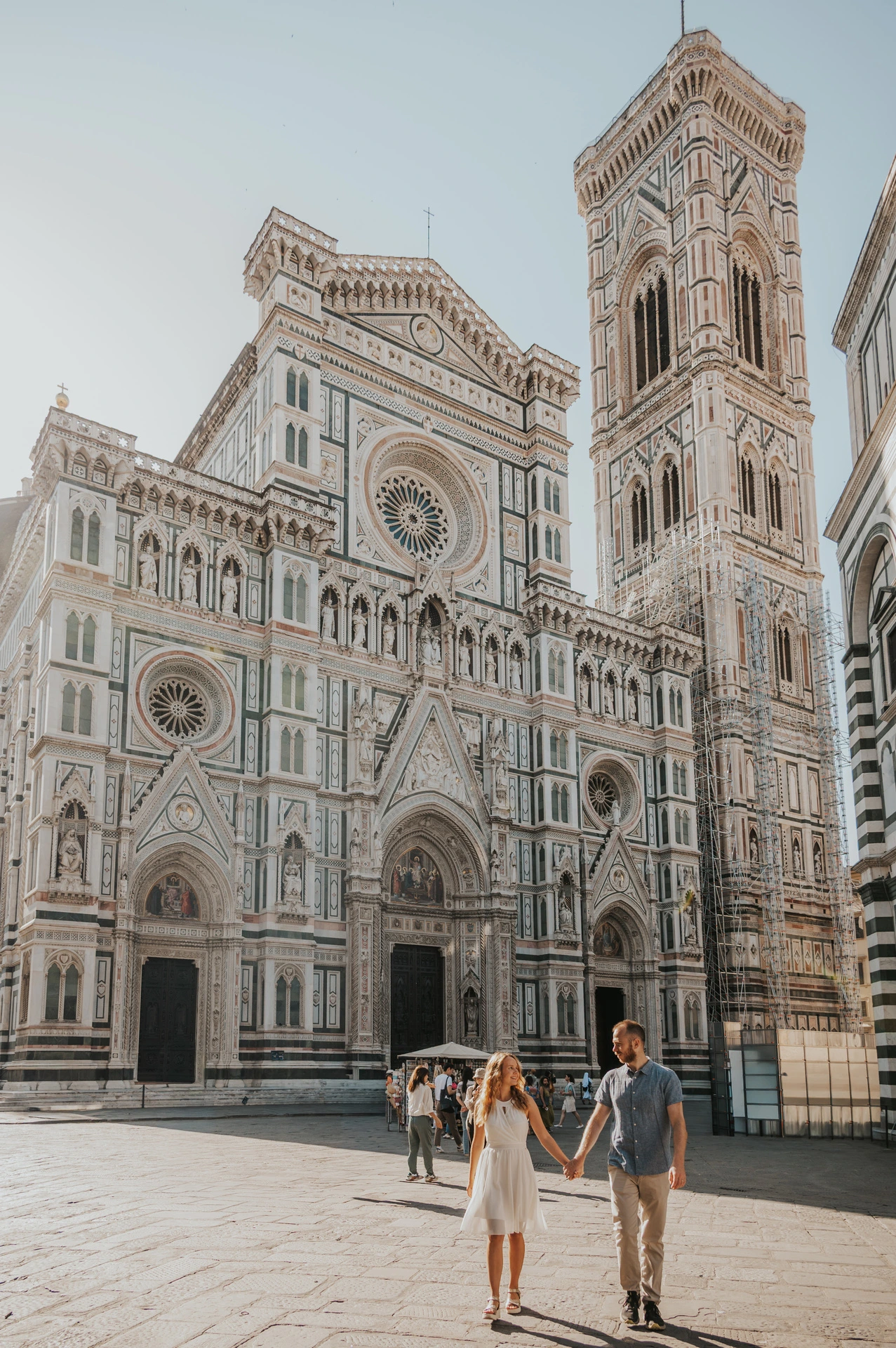 The couple walk across the square with Florence’s Duomo and bell tower towering behind them during their couple photoshoot.