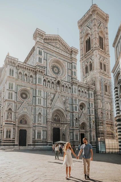 The couple walk across the square with Florence’s Duomo and bell tower towering behind them during their couple photoshoot.