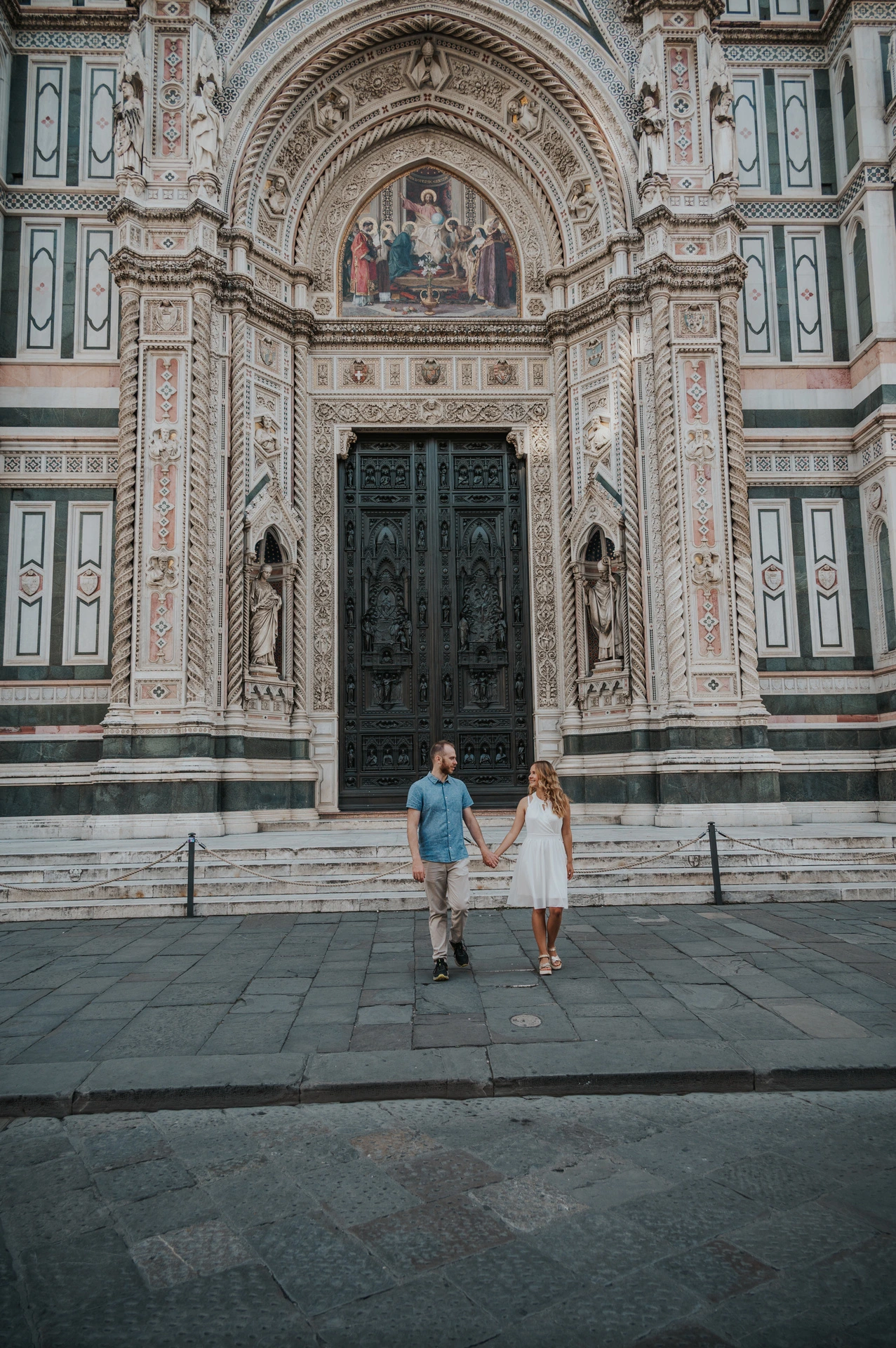 The couple walk hand in hand below the Duomo’s large carved doorway and patterned marble during their Florence photoshoot.